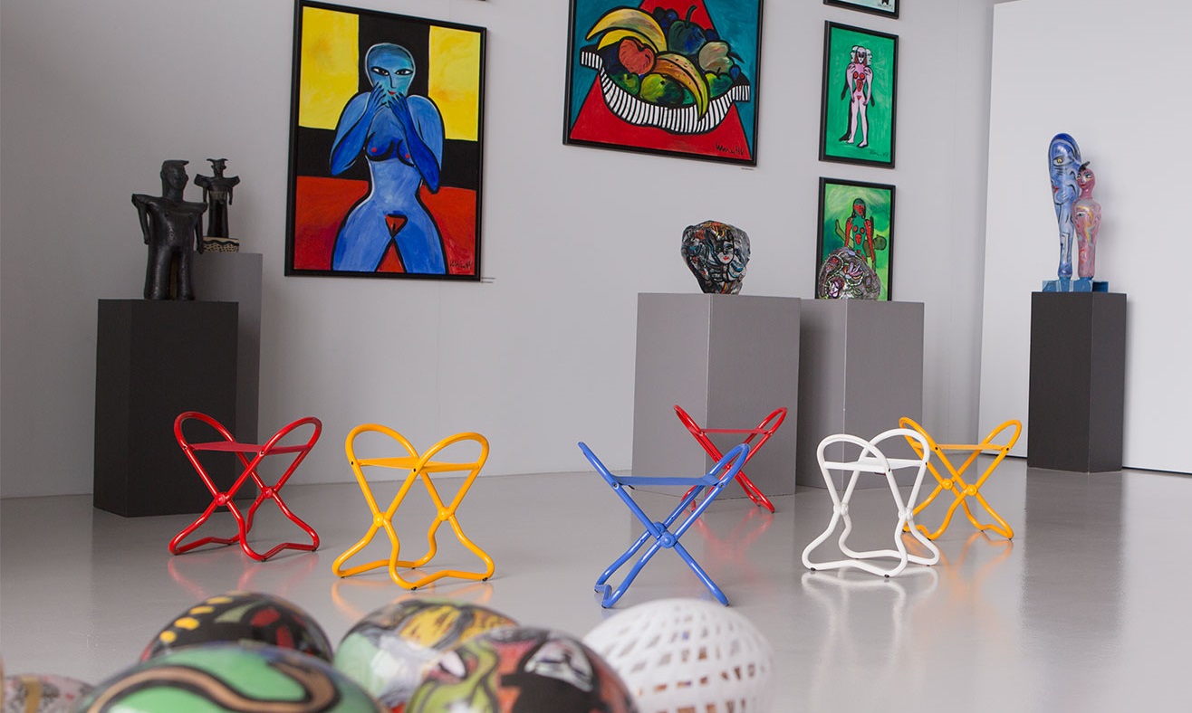 Ausstellung mit bunten Hockern, abstrakten Gemälden und Skulpturen im modernen Kunststil.