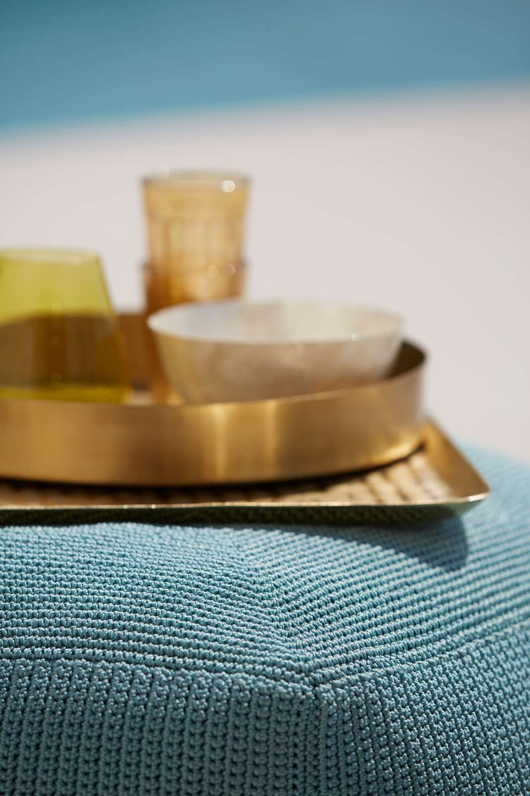 Nahaufnahme des Cane-Line Divine Outdoor Hockers in Sand mit Tablett und Gläsern.