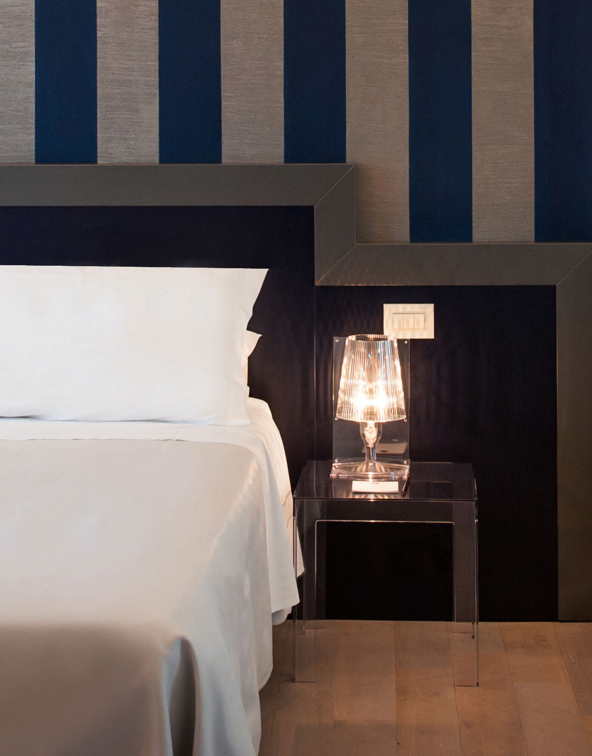 Nachttisch mit Lampe neben einem Bett. Kartell Jolly Beistelltisch aus transparentem Kunststoff.