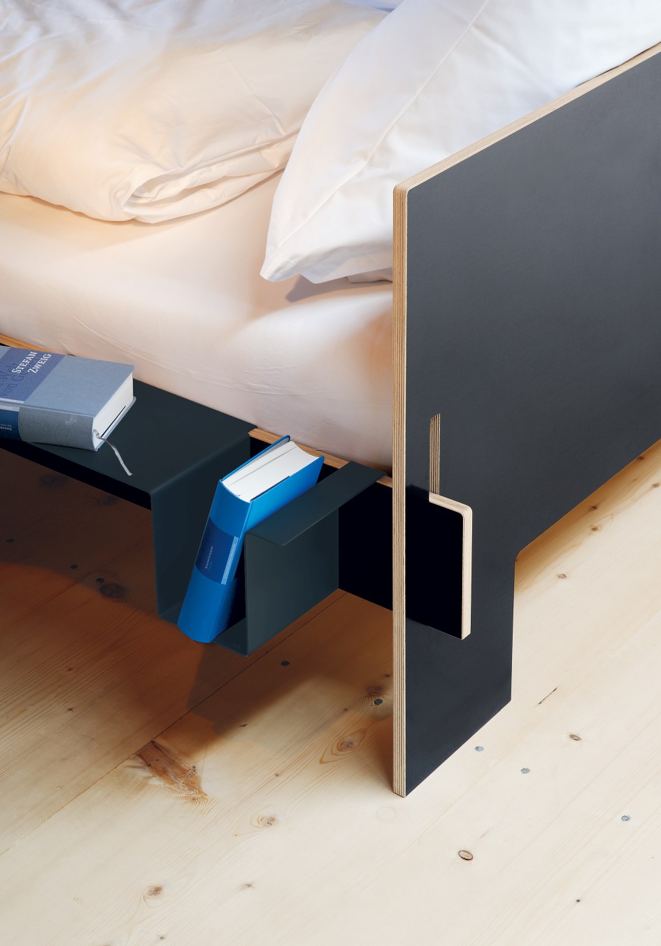 Anthrazitfarbene Seitenablage für Siebenschläfer Bett von Moormann mit Büchern auf hellem Holzboden.