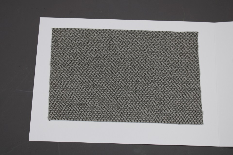 Stoffmusterkarte Gruppe 91 Cor: Nahaufnahme eines grauen, gewebten Textil-Musters für Möbelstoffe und Polster.