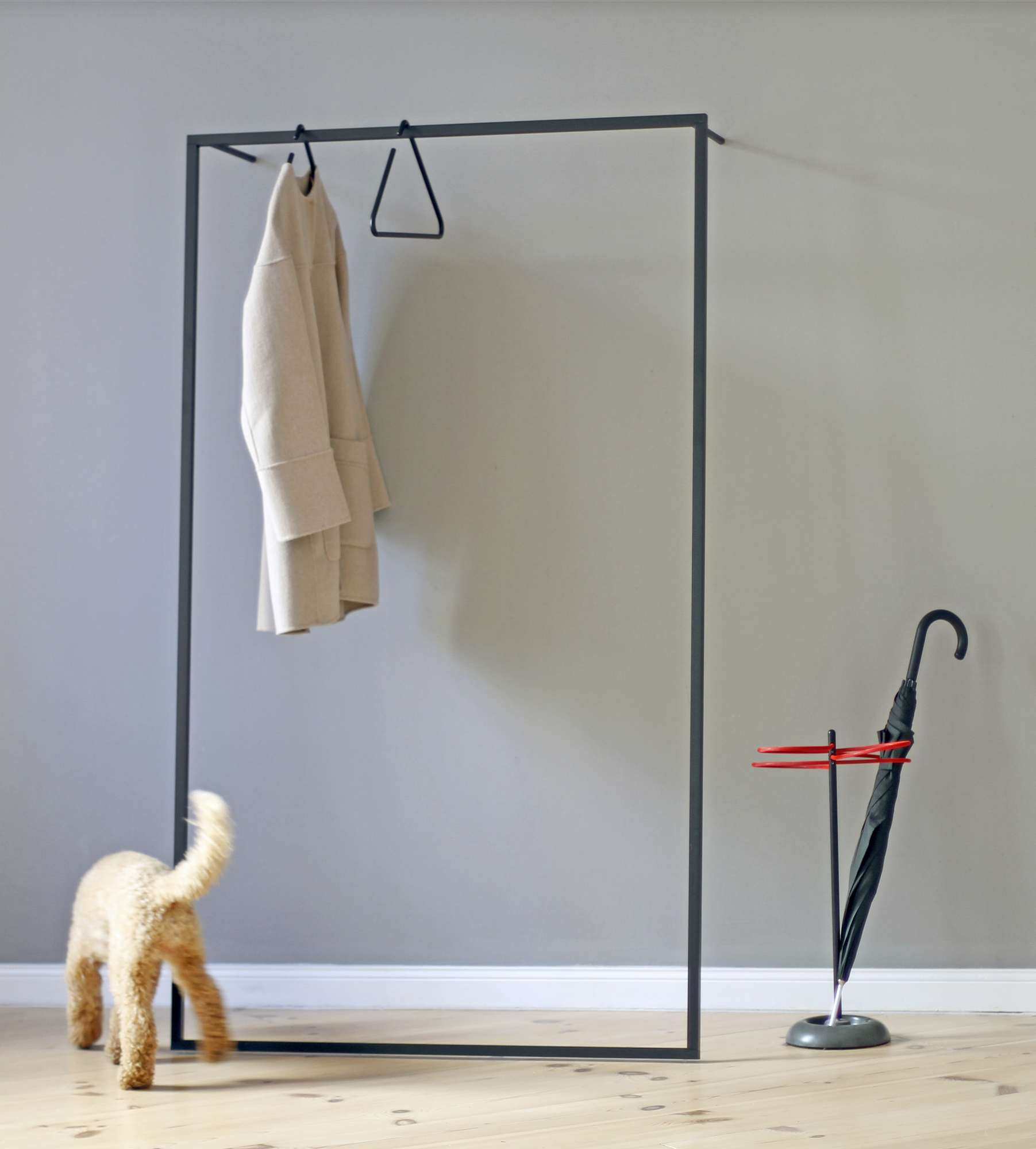 Leano Anlehngarderobe von Roomsafari mit Mantel, Schirmständer und Hund im Flur. Moderne Garderobenlösung.