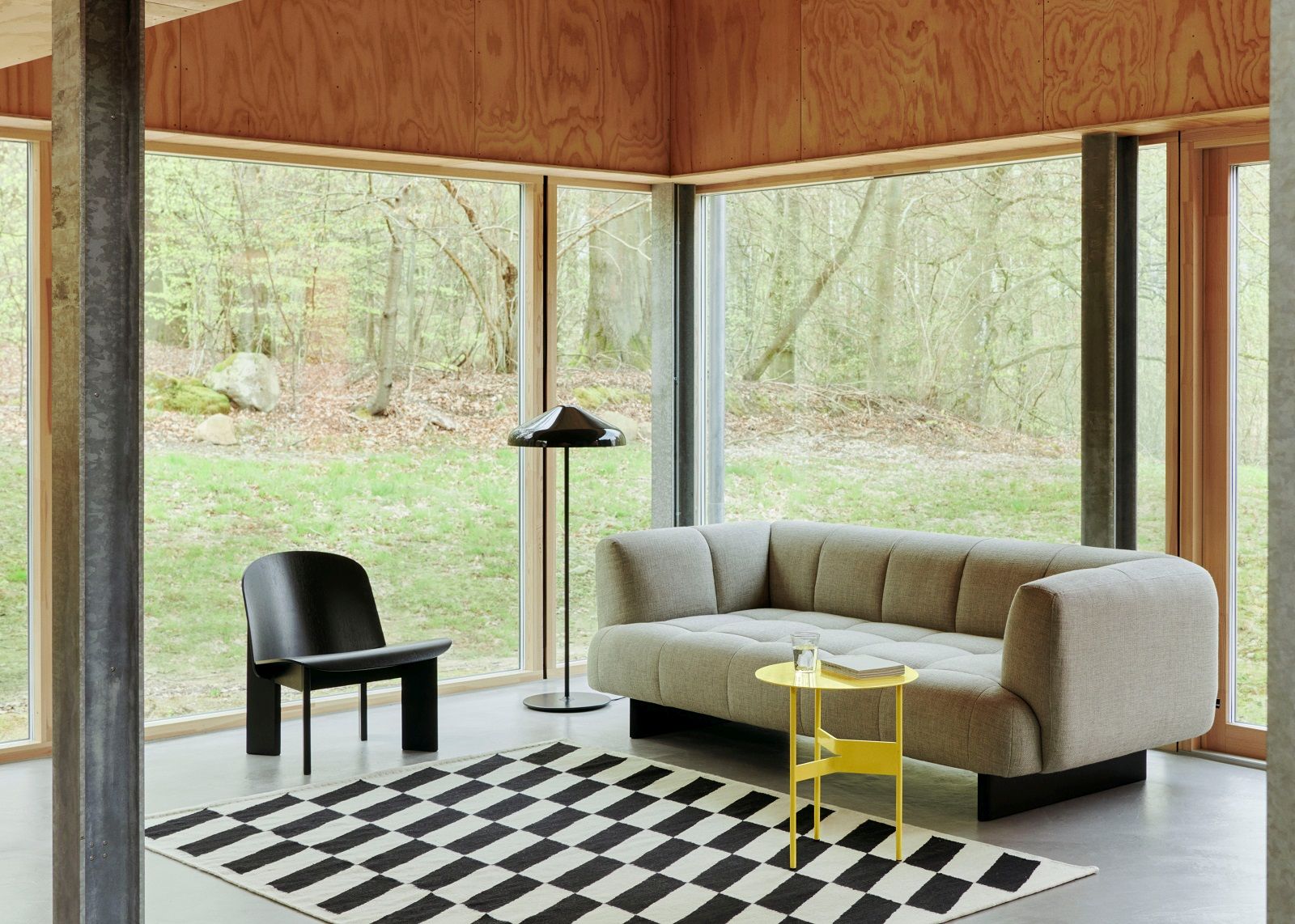 Wohnzimmer mit Sofa, Stuhl, Lampe und Hay Kelim Teppich mit Schachbrettmuster in Schwarz-Weiß.