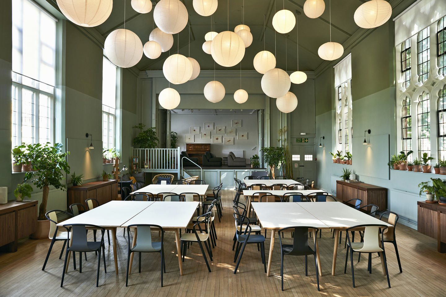 Helle Halle mit Tischen und Belleville Stühlen mit Holzschale und schwarzem Gestell.