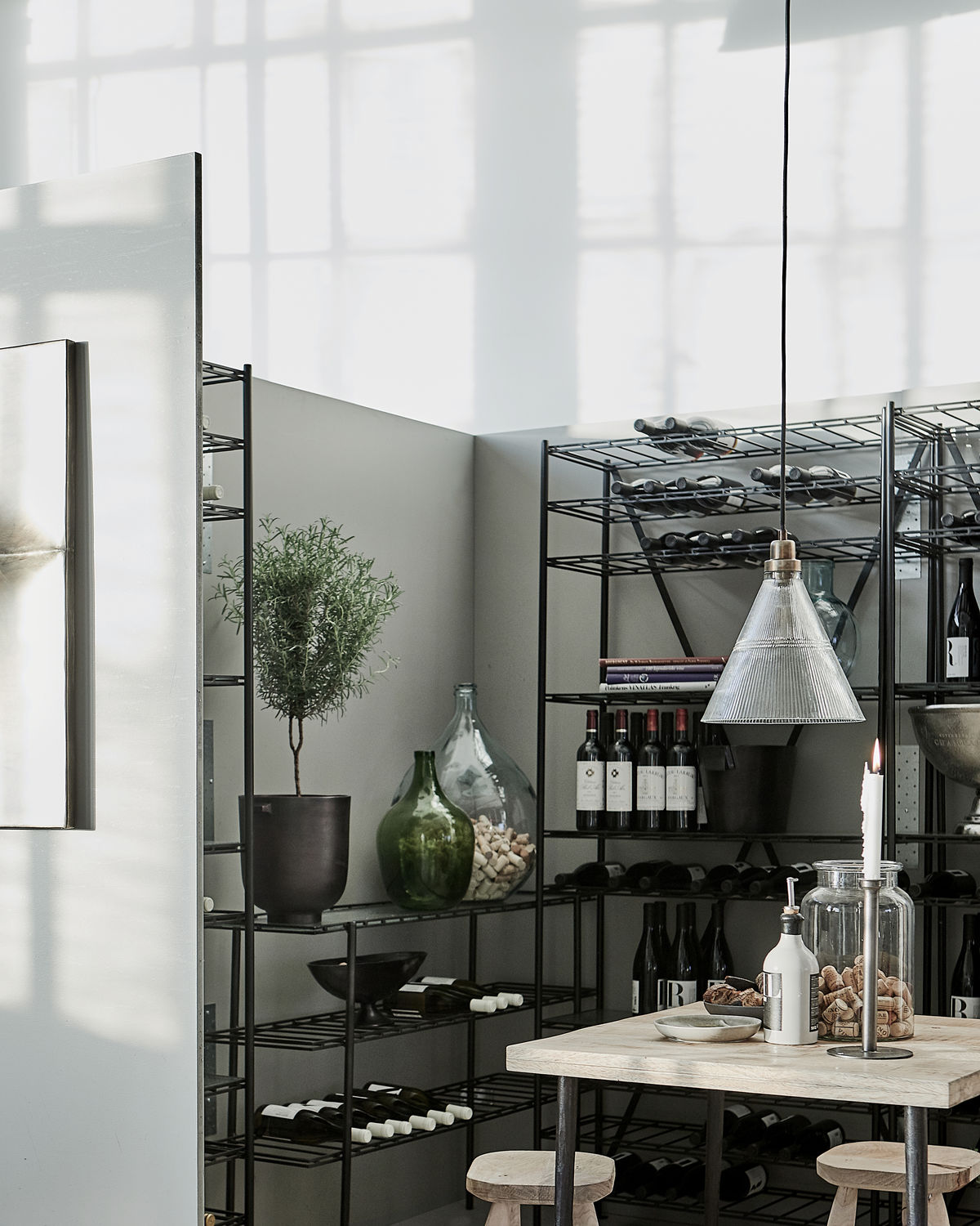 Vira Pendelleuchte von House Doctor über Esstisch mit Weinflaschen im Hintergrund, moderne Innenraumbeleuchtung.