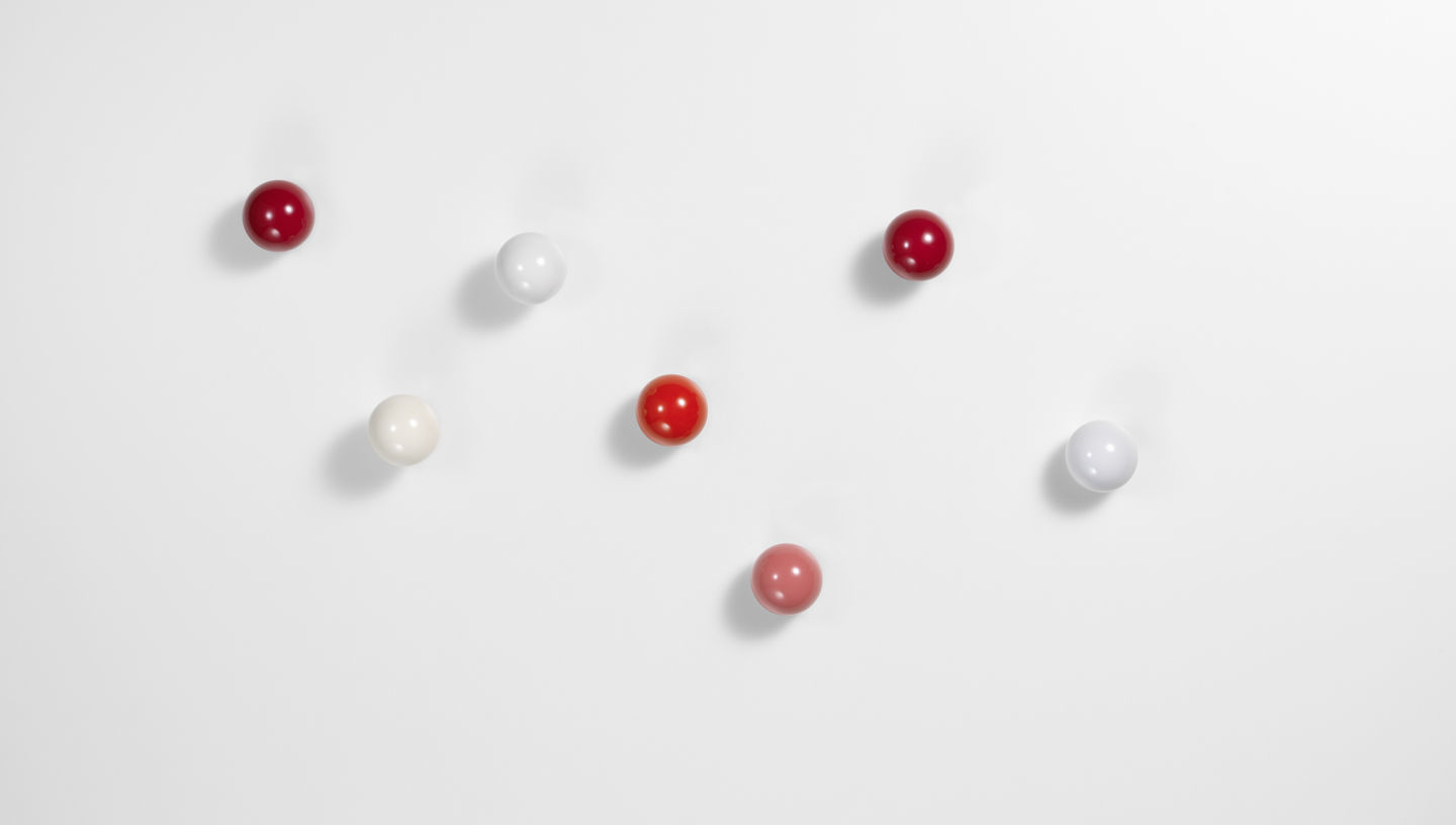 Vitra Coat Dots Garderobenhaken 3er-Set in Rot- und Weißtönen an einer weißen Wand.