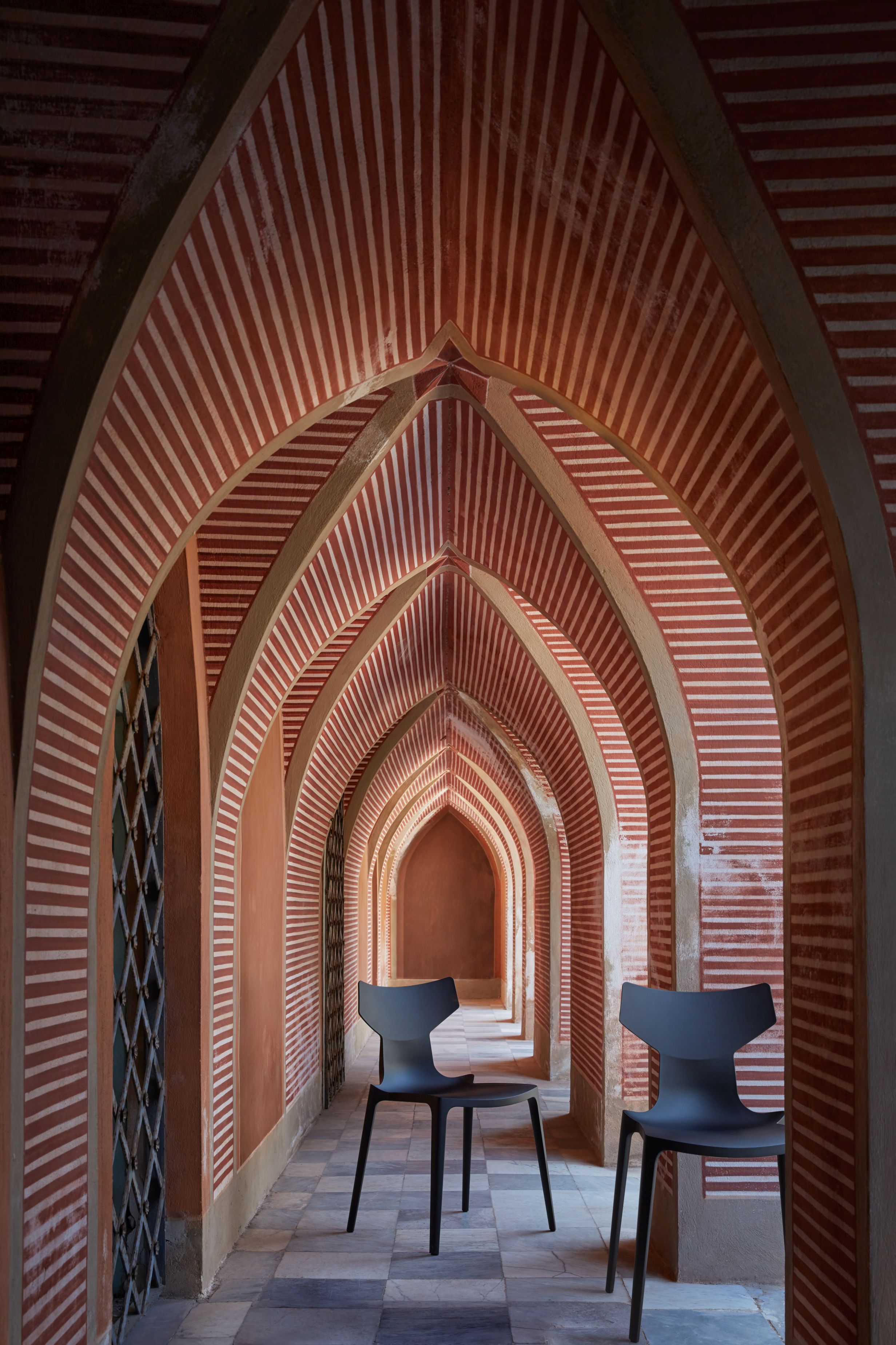 Zwei schwarze Re-Chair Stühle von Kartell in einem Gang mit roten Bögen. Designermöbel.