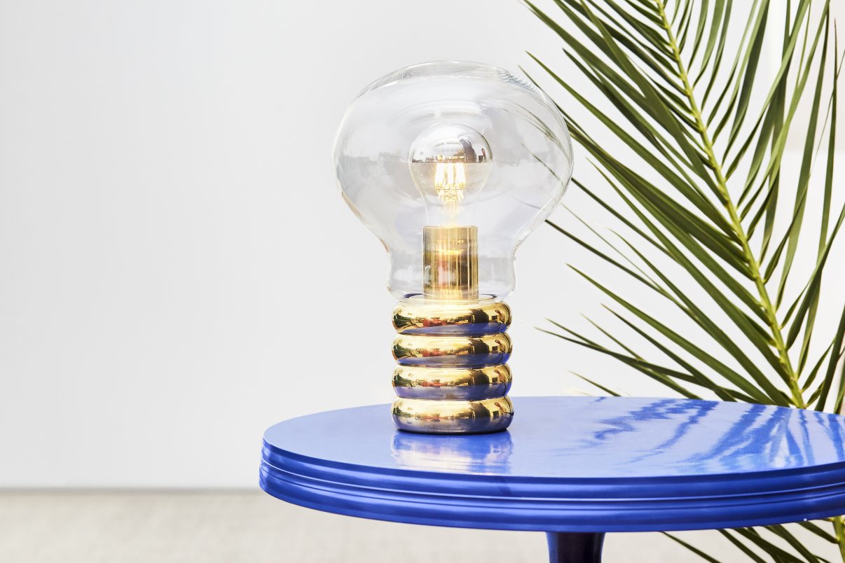 Detailaufnahme der Ingo Maurer Bulb Tischleuchte mit Messingfuß und Glühbirnen-Design auf blauem Tisch.
