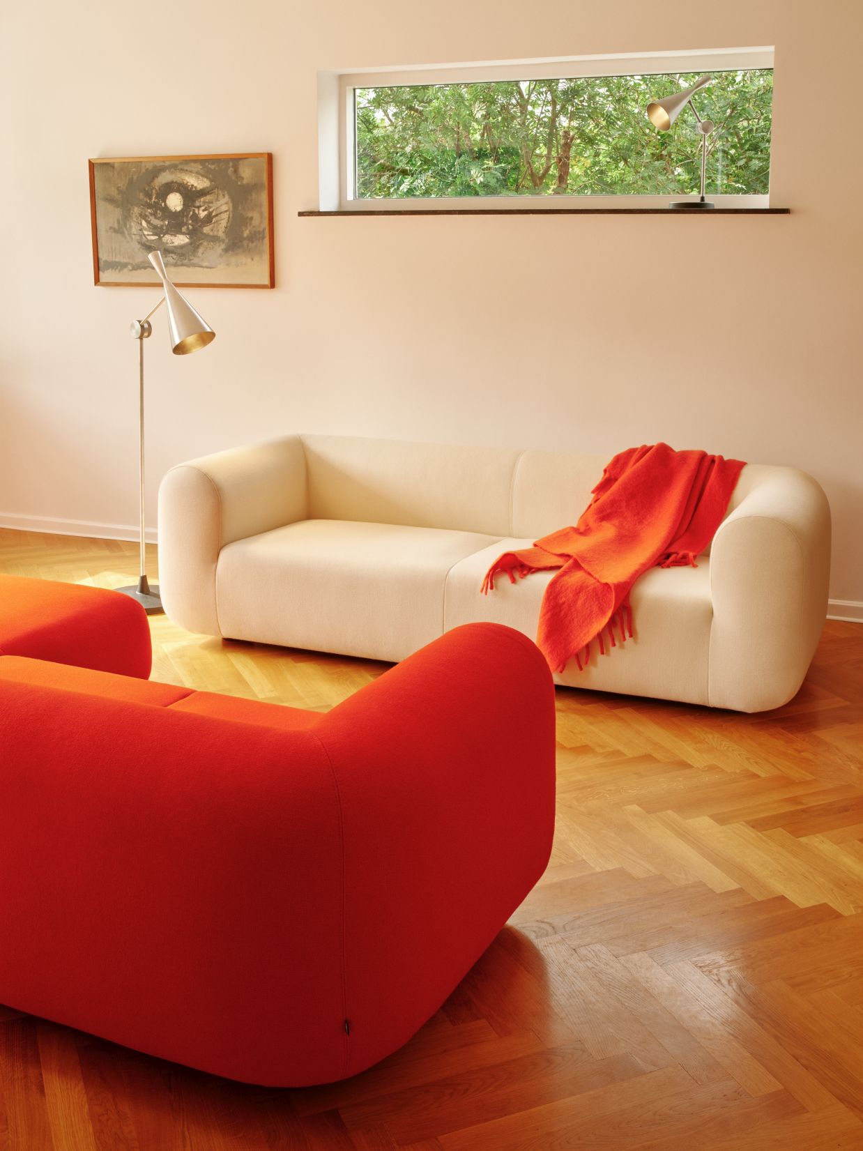 Wohnzimmer mit Tom Dixon Unbeaten Stehleuchte, weißem Sofa mit orangefarbener Decke und roten Sesseln.