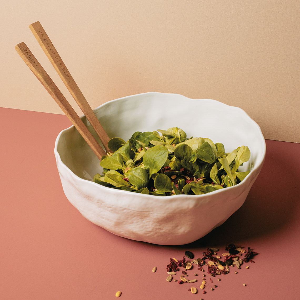 Weiße Räder Geniesser Schale gefüllt mit frischem Salat und hölzernem Salatbesteck. Dekorative Keramikschale.
