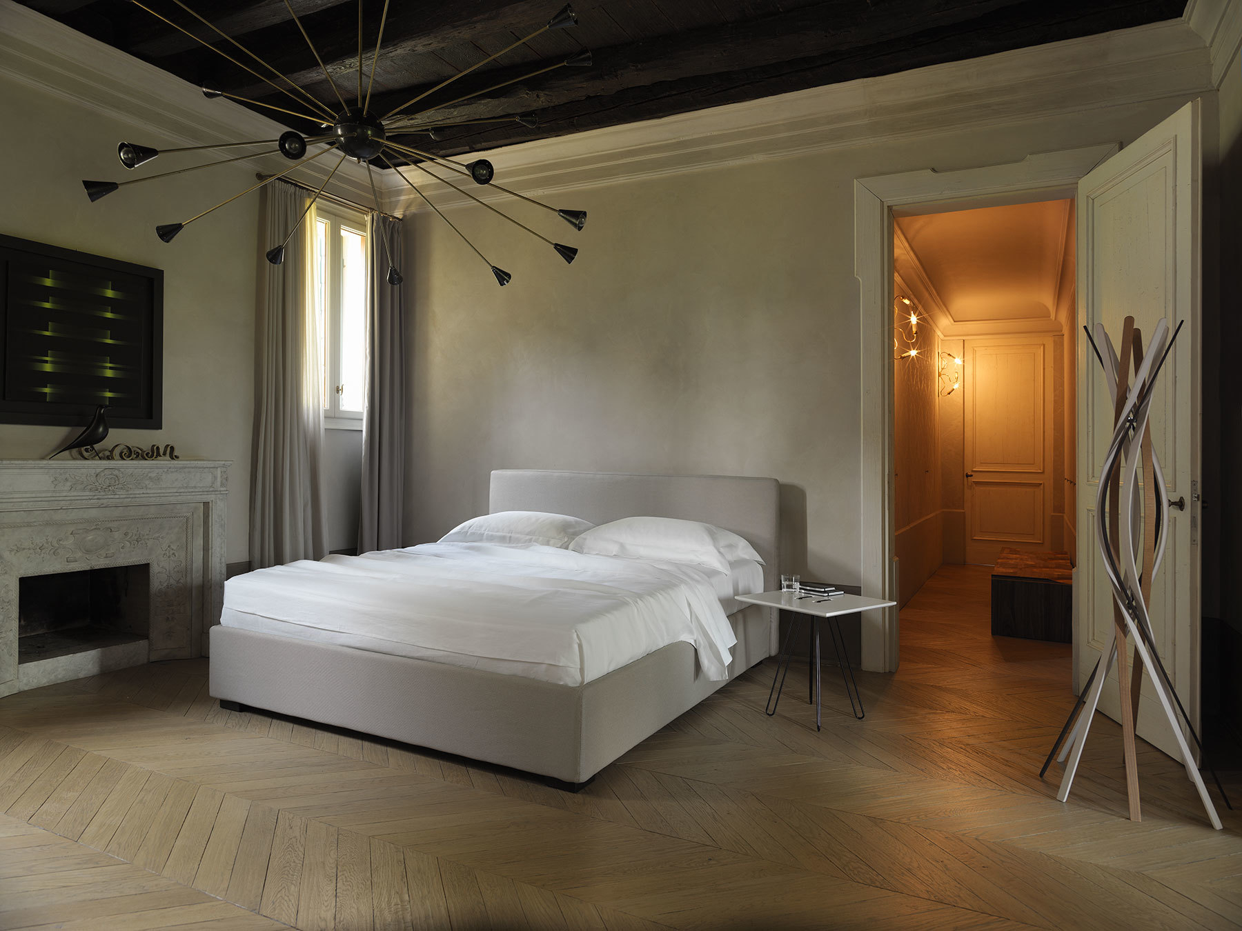 Casamania Horm Twist Garderobenständer aus Holz im Schlafzimmer mit Bett und Parkettboden.