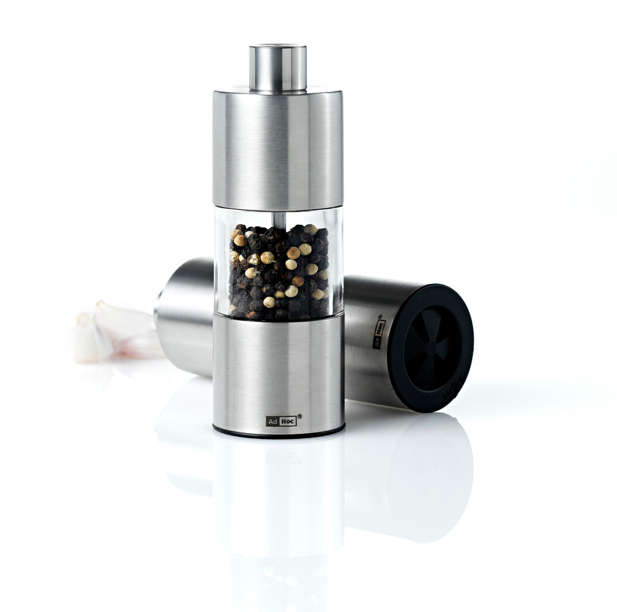 AdHoc Pfeffermühle aus Edelstahl, gefüllt mit Pfefferkörnern, neben liegender Salzmühle auf weißem Hintergrund.