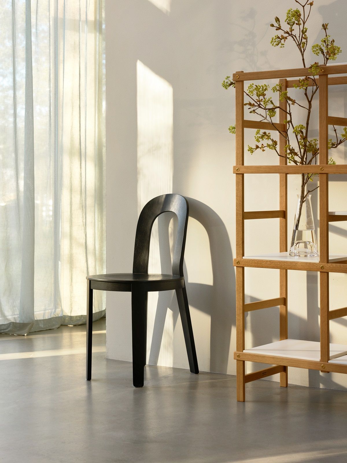 Schwarzer Olivia Chair Holzstuhl von Design House Stockholm neben einem Holzregal im hellen Raum.