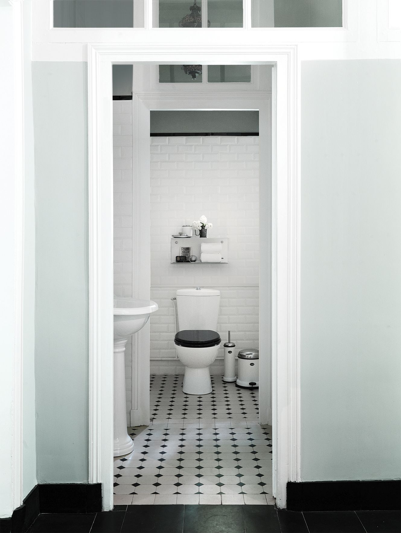 Helles Badezimmer mit weißer Toilette, Vipp WC-Bürste und Mülleimer auf einem schwarz-weiß gemusterten Boden.