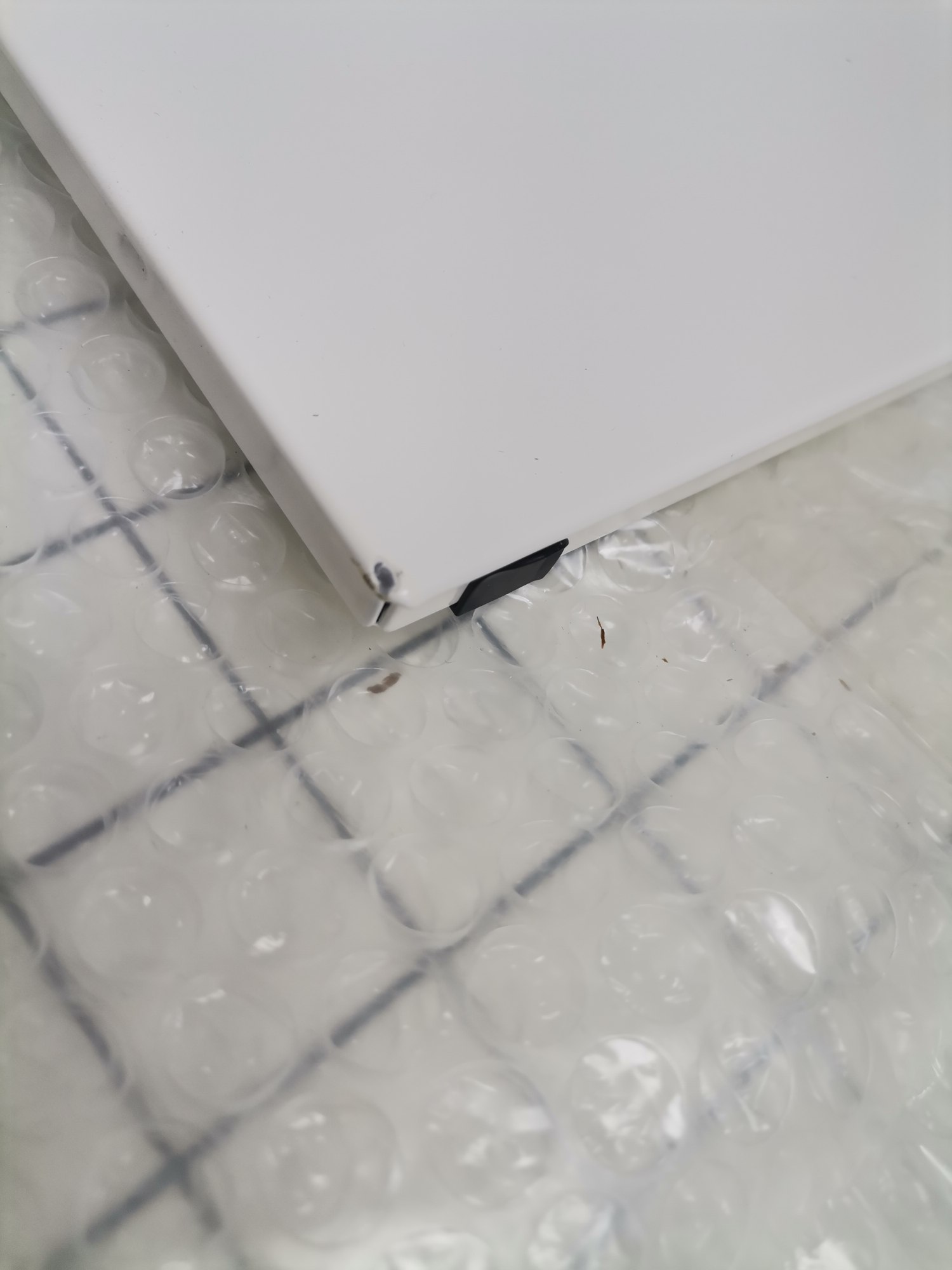 Detailaufnahme eines weißen USM Haller Ersatzteils mit Beschädigung, verpackt in Luftpolsterfolie.