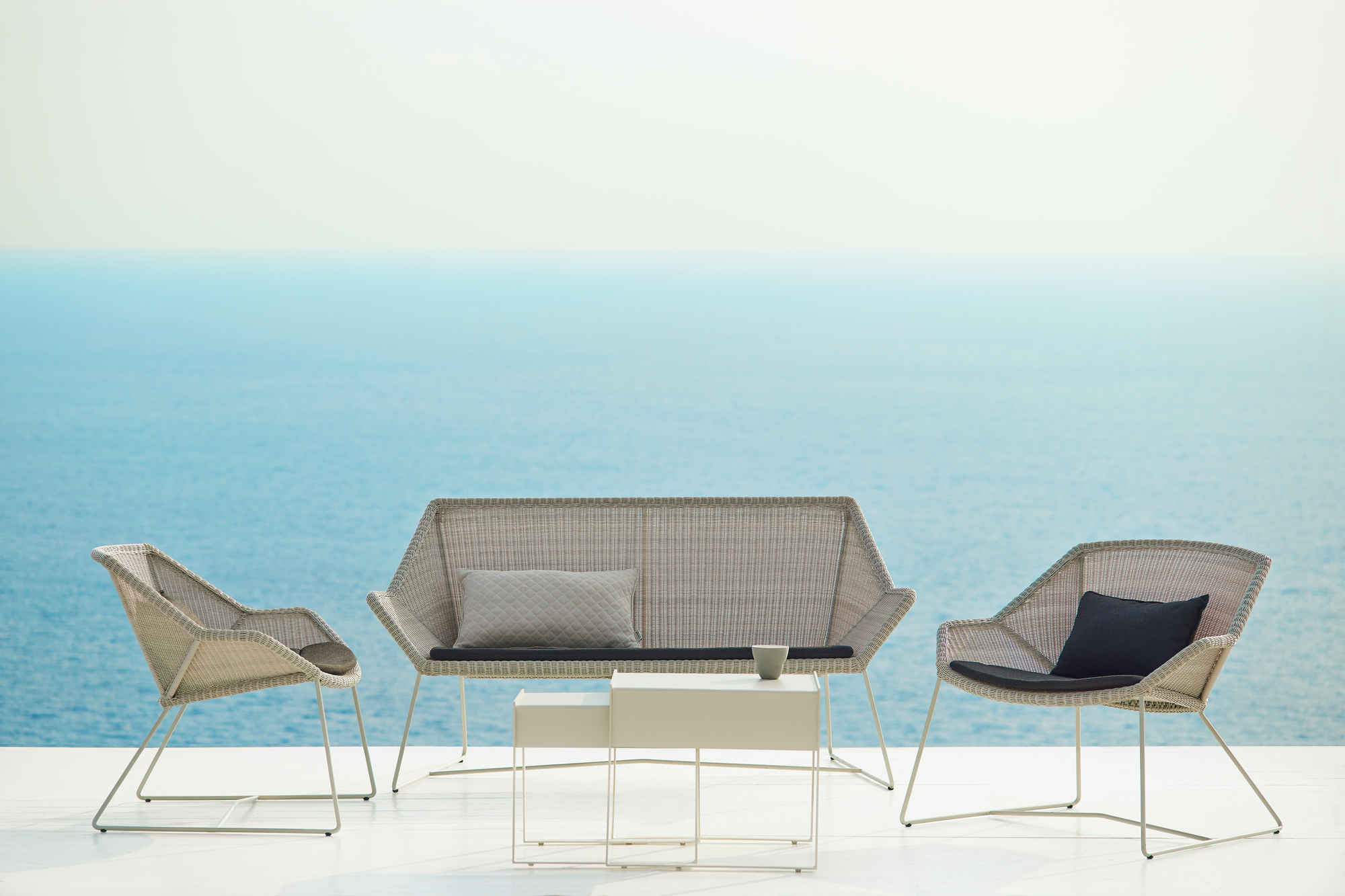 Breeze Loungesessel und Sofa von Cane-Line: Moderne Outdoor-Möbel aus Rattan mit Kissen vor Meer.