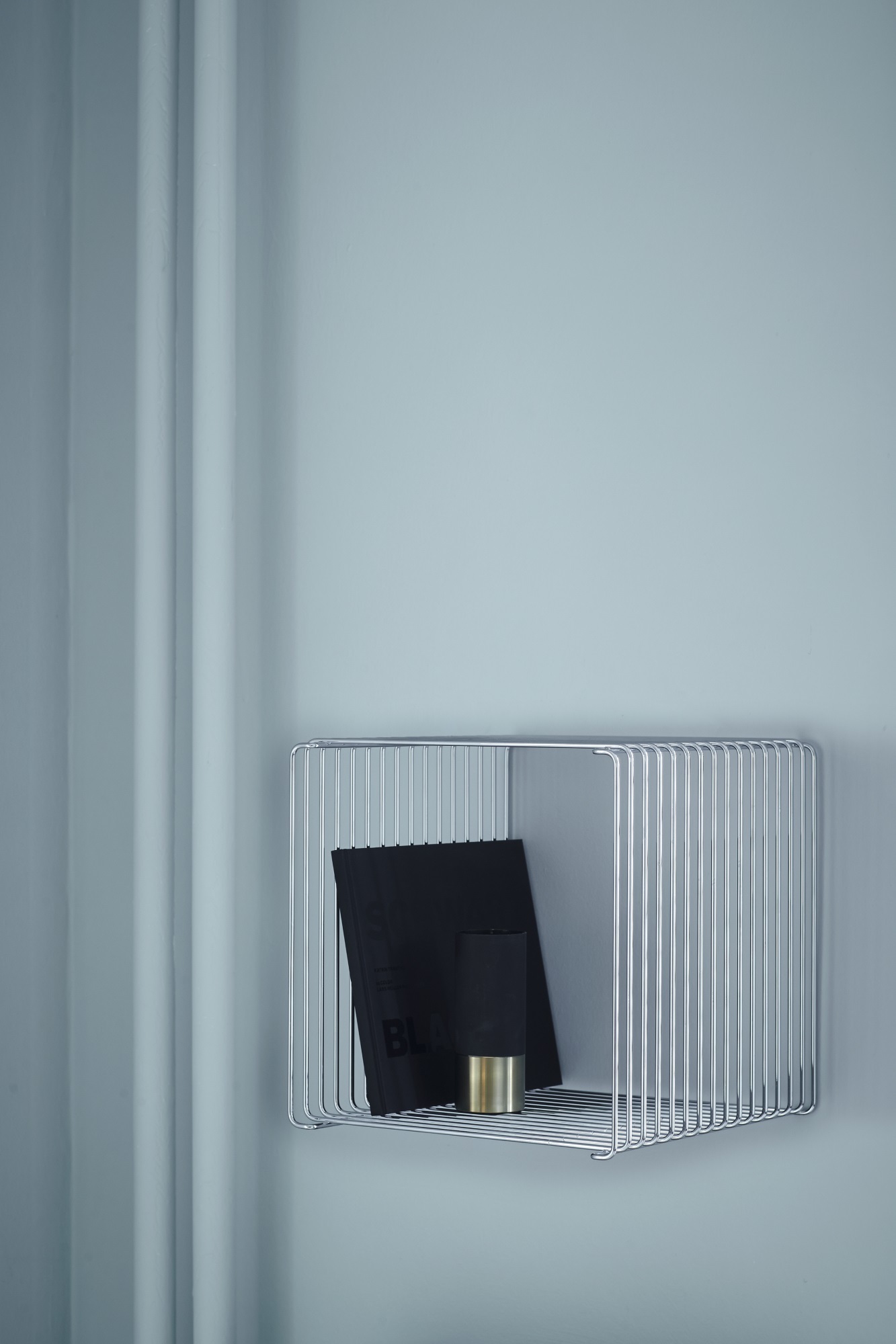 Montana Wire Cube Regal aus verchromtem Draht mit Buch und Dekoration an hellblauer Wand.