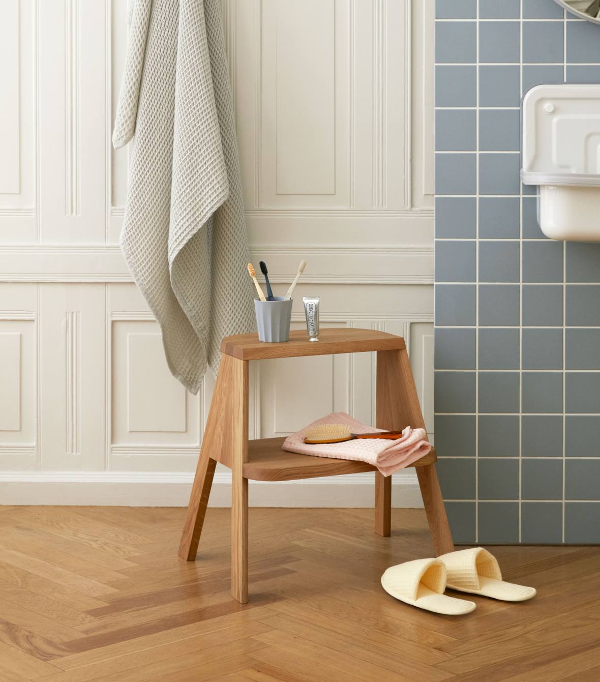 Hay Butler Hocker aus Holz im Badezimmer mit Handtuch, Zahnbürsten und Badeschuhen.