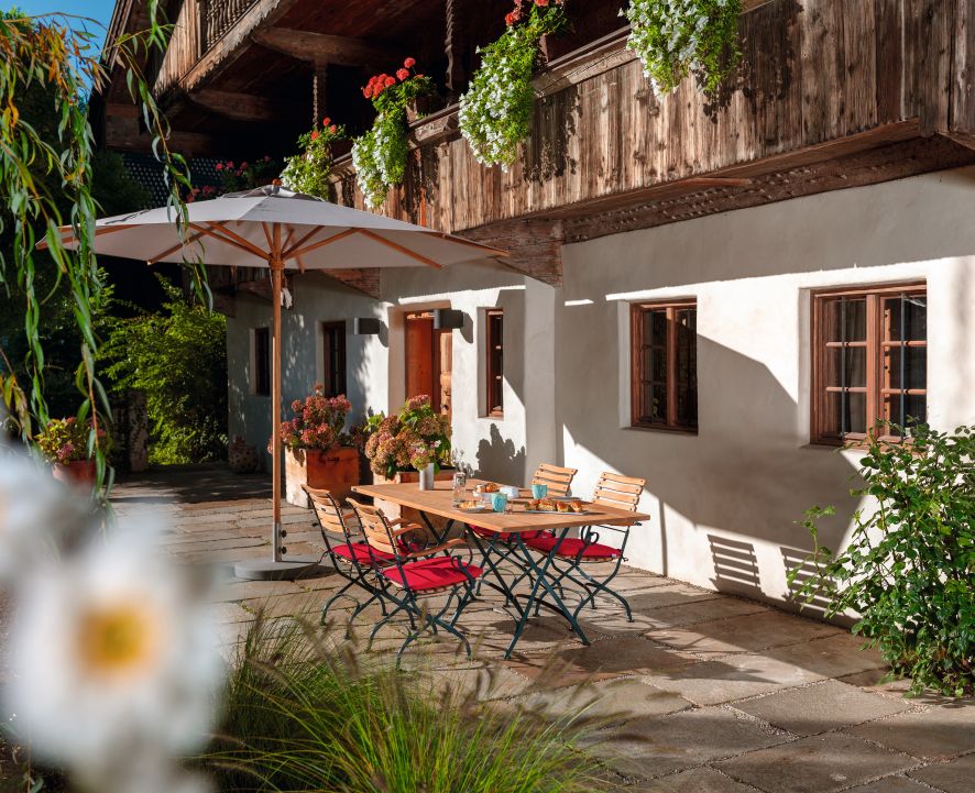 Weishäupl Classic Tisch 120 cm Outdoor Weiß mit Stühlen und Sonnenschirm auf Terrasse.