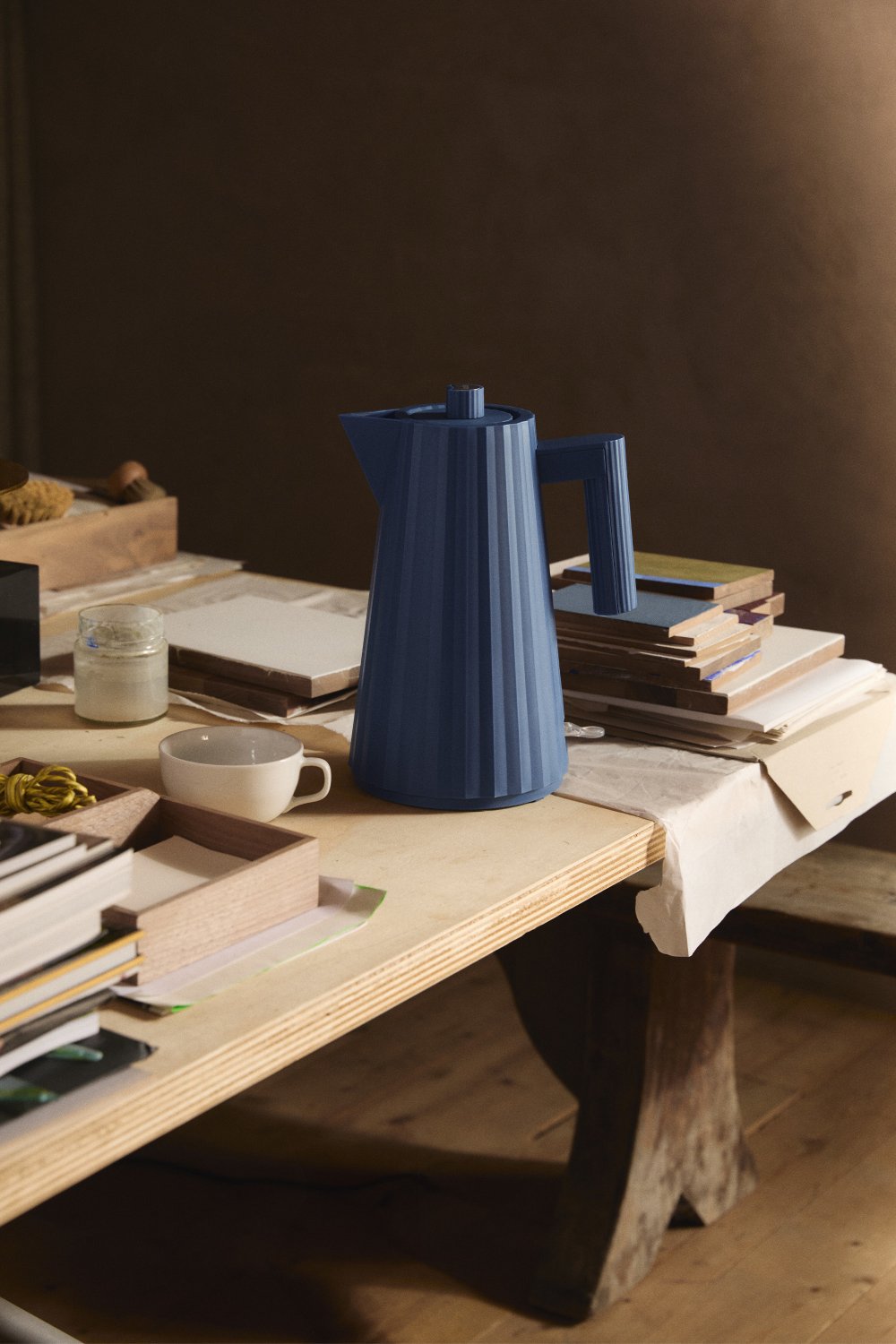 Blauer Alessi Plissé Wasserkocher MDL06 auf einem Tisch mit Tasse und Büchern.