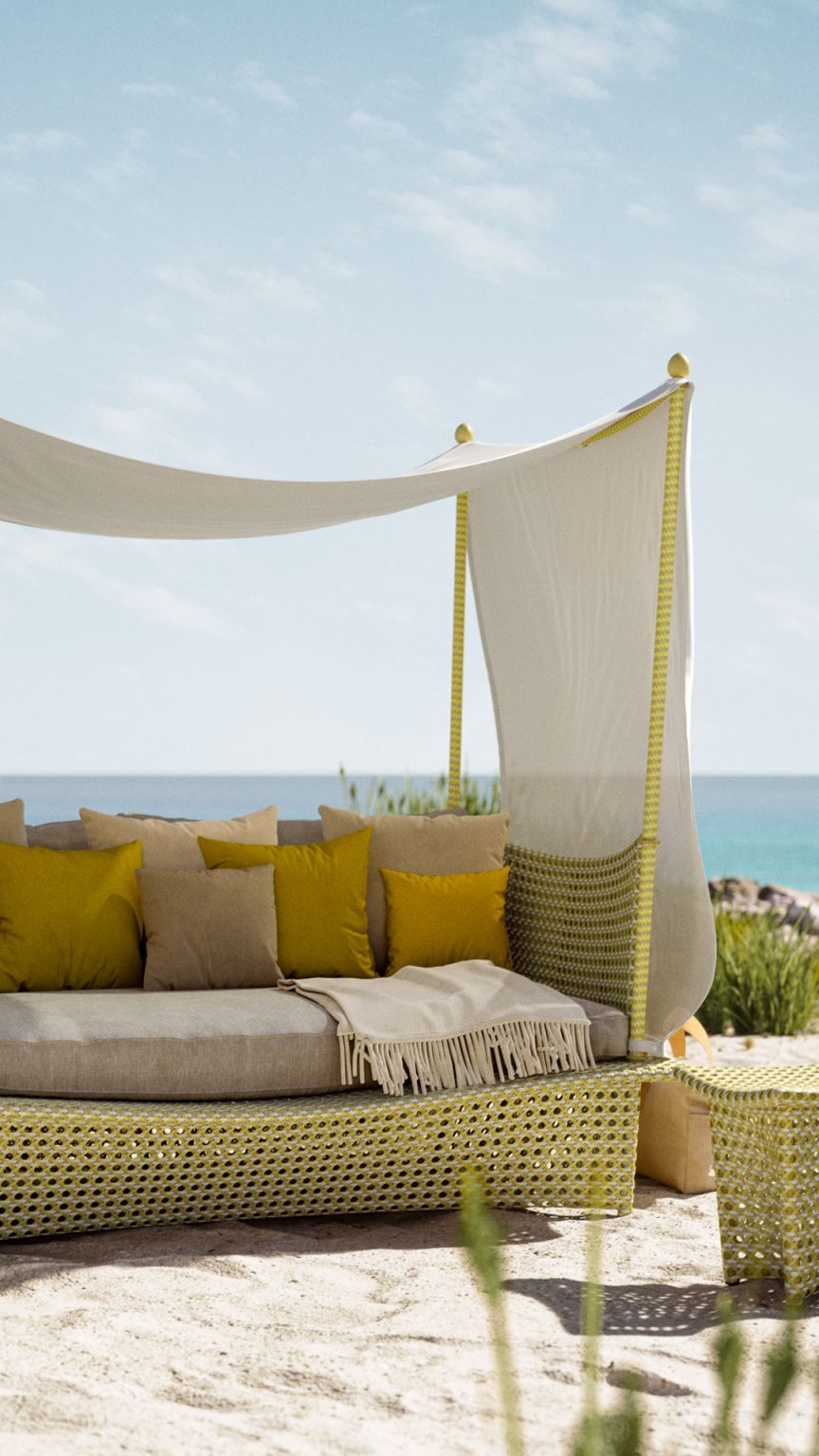 Daydream Beistelltisch von Dedon: Gelbes Outdoor-Daybed mit Baldachin, Kissen und Beistelltisch am Strand.