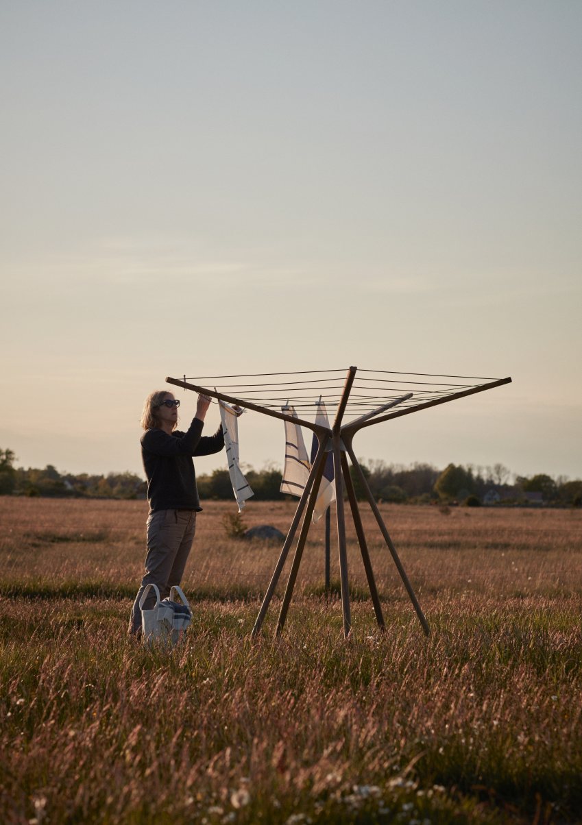 Frau hängt Wäsche auf dem Skagerak Spider Web Wäscheständer im Freien auf.