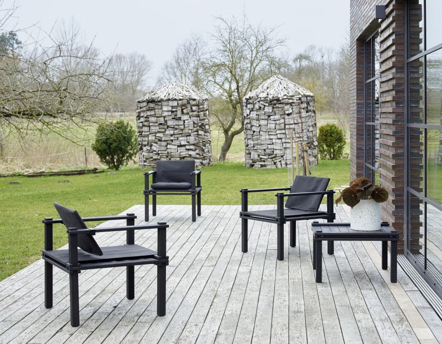 Drei schwarze Outdoor Sessel und ein Farmer Tisch auf einer Holzterrasse im Garten.