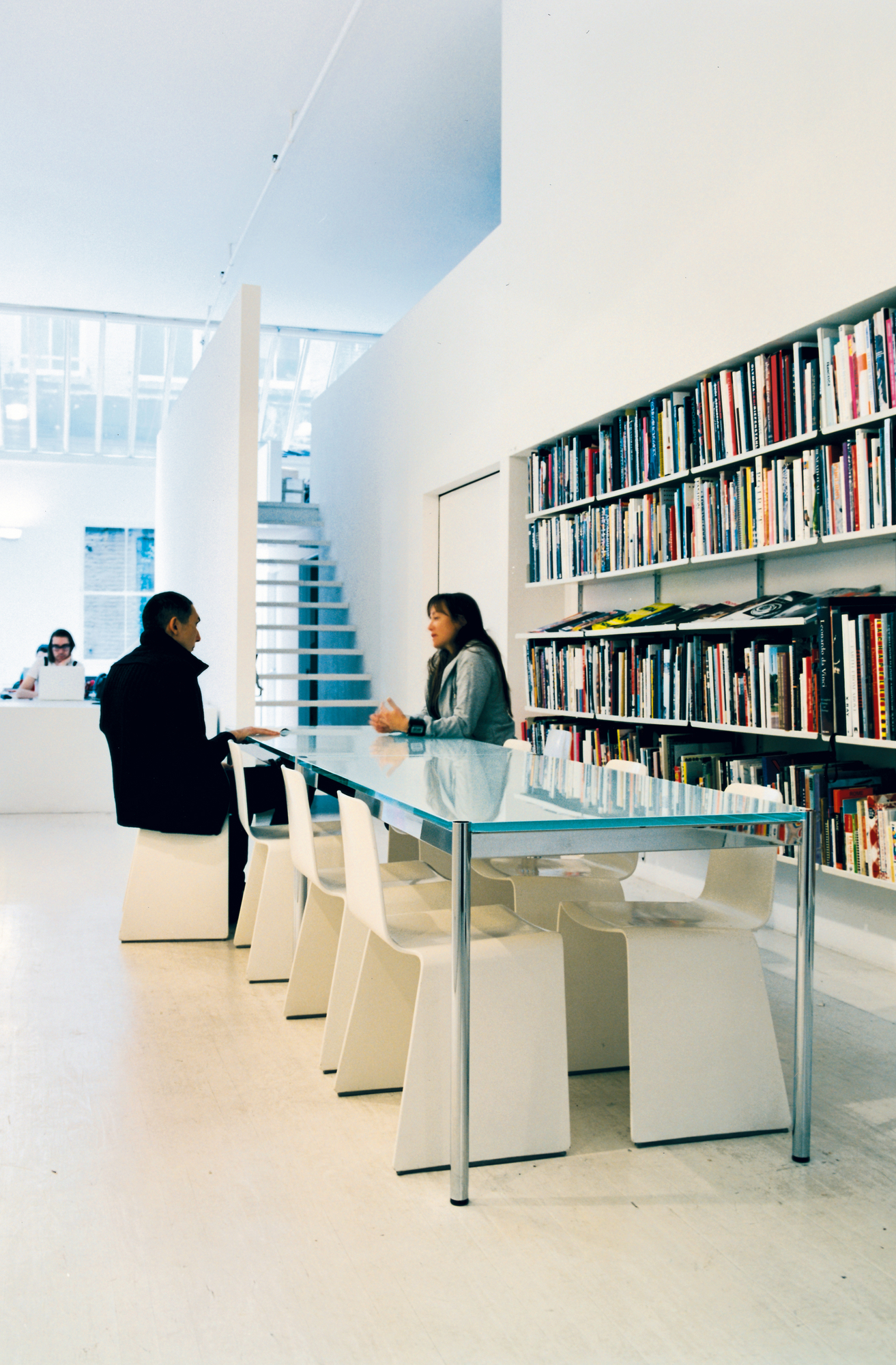 USM Haller Tisch mit Glasplatte, 175x100 cm, in einem hellen Büro mit Personen und Bücherregal.