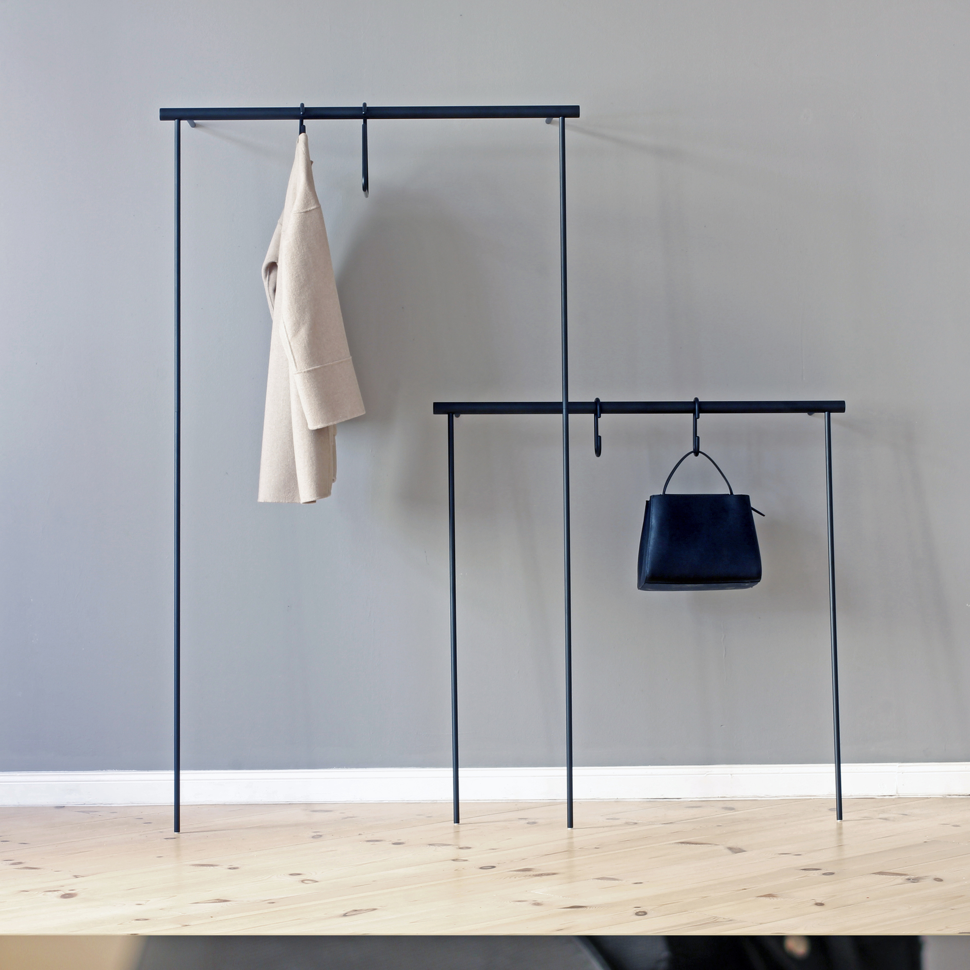 Leanon II Anlehngarderobe von Roomsafari: Moderne Garderobe mit Mantel und Handtasche an Stangen.