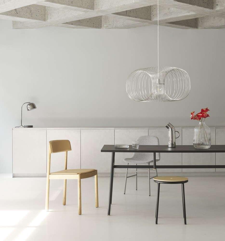Normann Copenhagen Coil Pendelleuchte über Esstisch mit Stühlen und minimalistischem Interieur. Moderne Hängelampe.