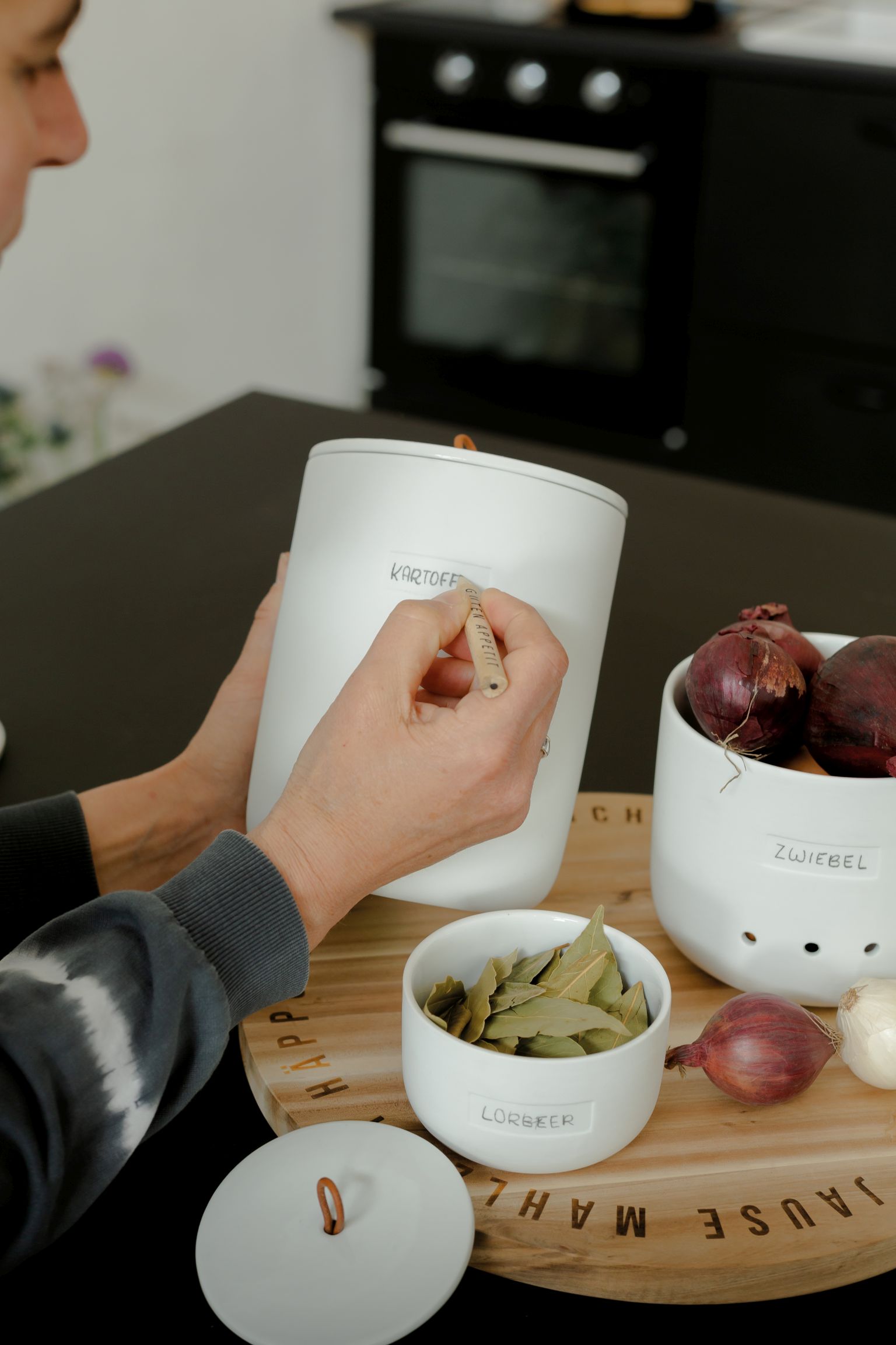 Person beschriftet weißen Vorratsbehälter. Keramik Aufbewahrungstopf für Kartoffeln, Zwiebeln und Lorbeerblätter. Küchenorganisation mit Stil.