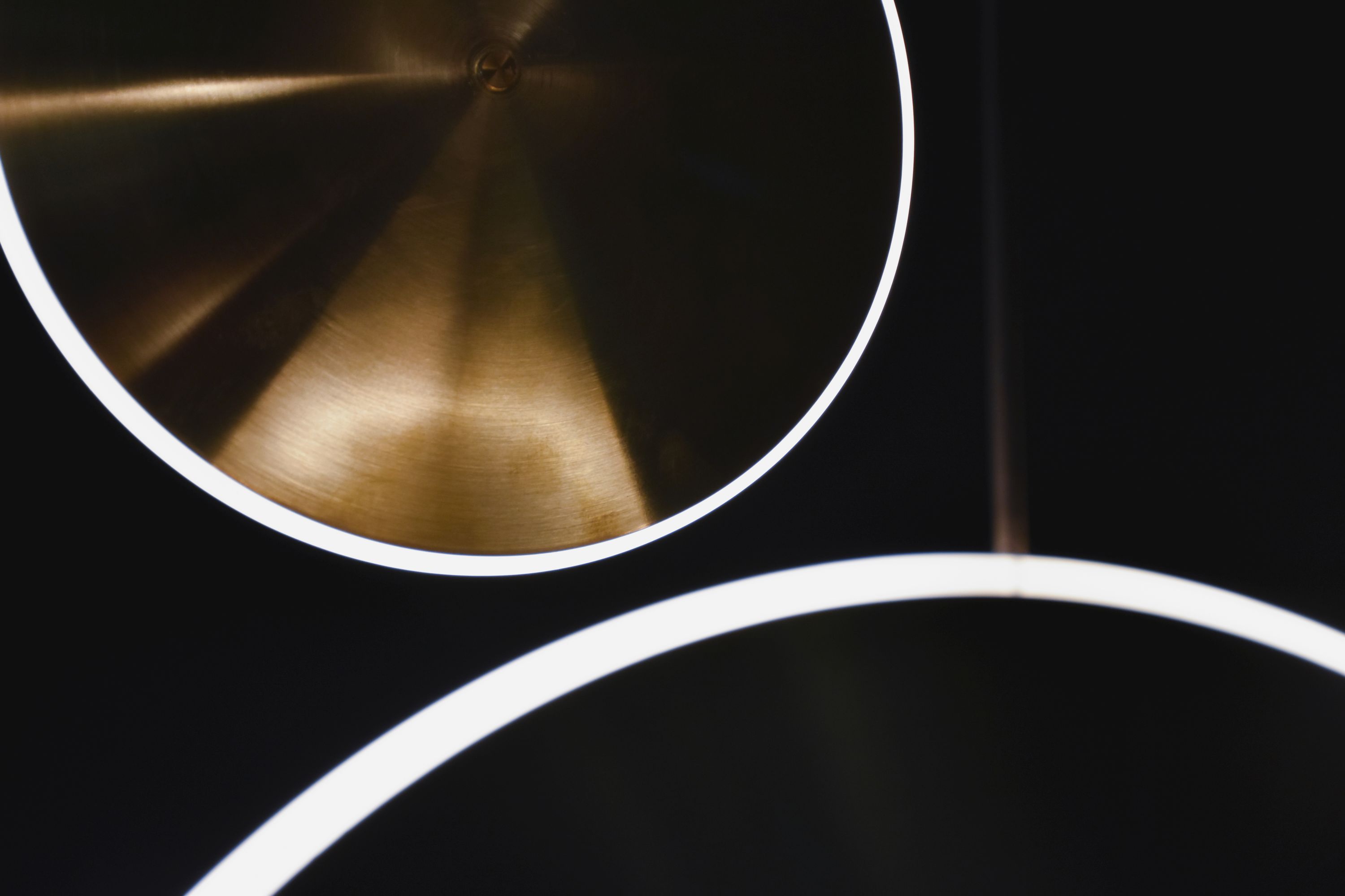 Detailaufnahme der Sconce10 Chrona Wandleuchte von Graypants: Messingfarbene Scheibe mit LED-Lichtring vor dunklem Hintergrund.