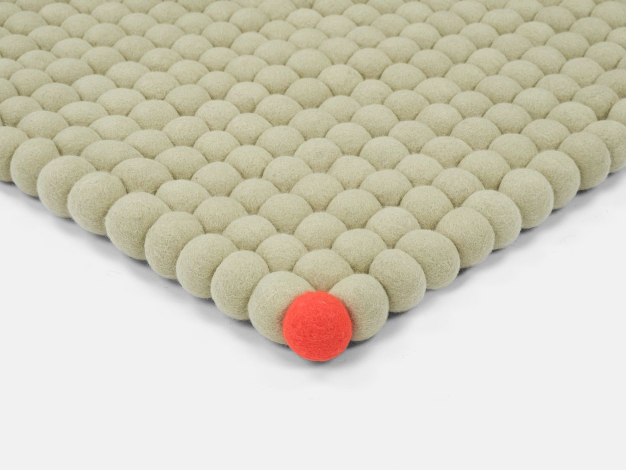 Detailaufnahme des Big One Filzteppichs in Grünbeige, 140x200 cm, mit roten Akzent. Filzkugelteppich für Wohnzimmer.