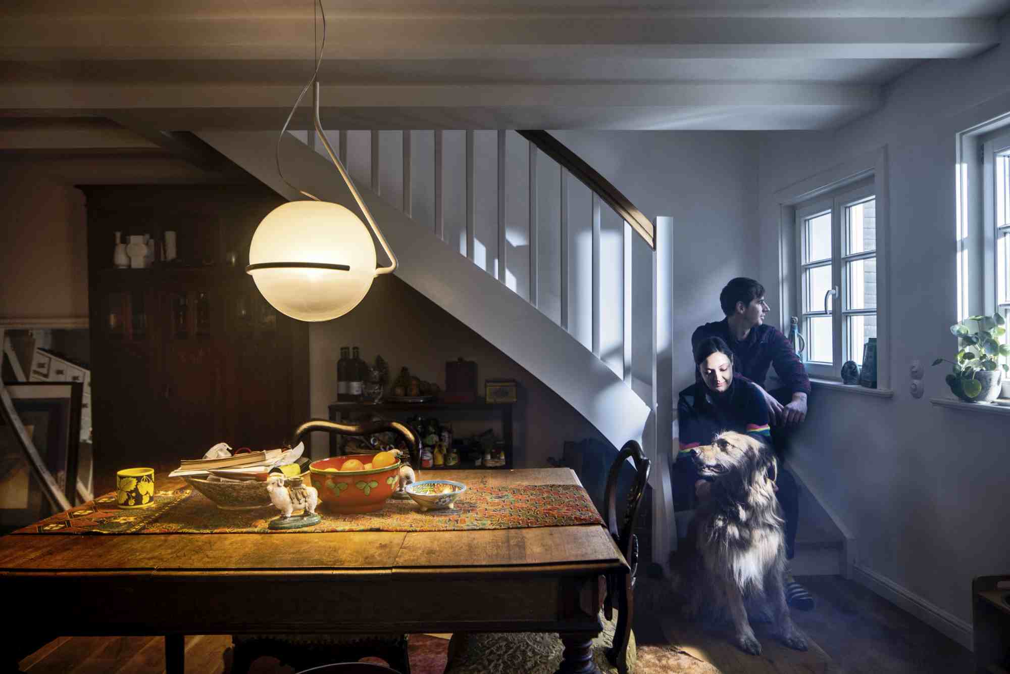 Helle Tonda Pendelleuchte von Foscarini über Esstisch in gemütlichem Wohnzimmer mit Paar und Hund.