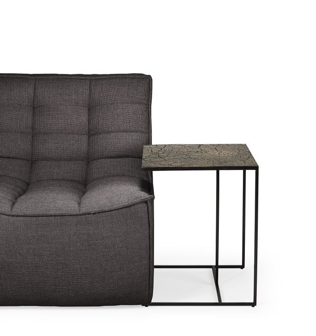 Ethnicraft Triptic Beistelltisch Whisky neben einem grauen Sofa, minimalistisches Design mit dunklem Holz und Metallgestell.