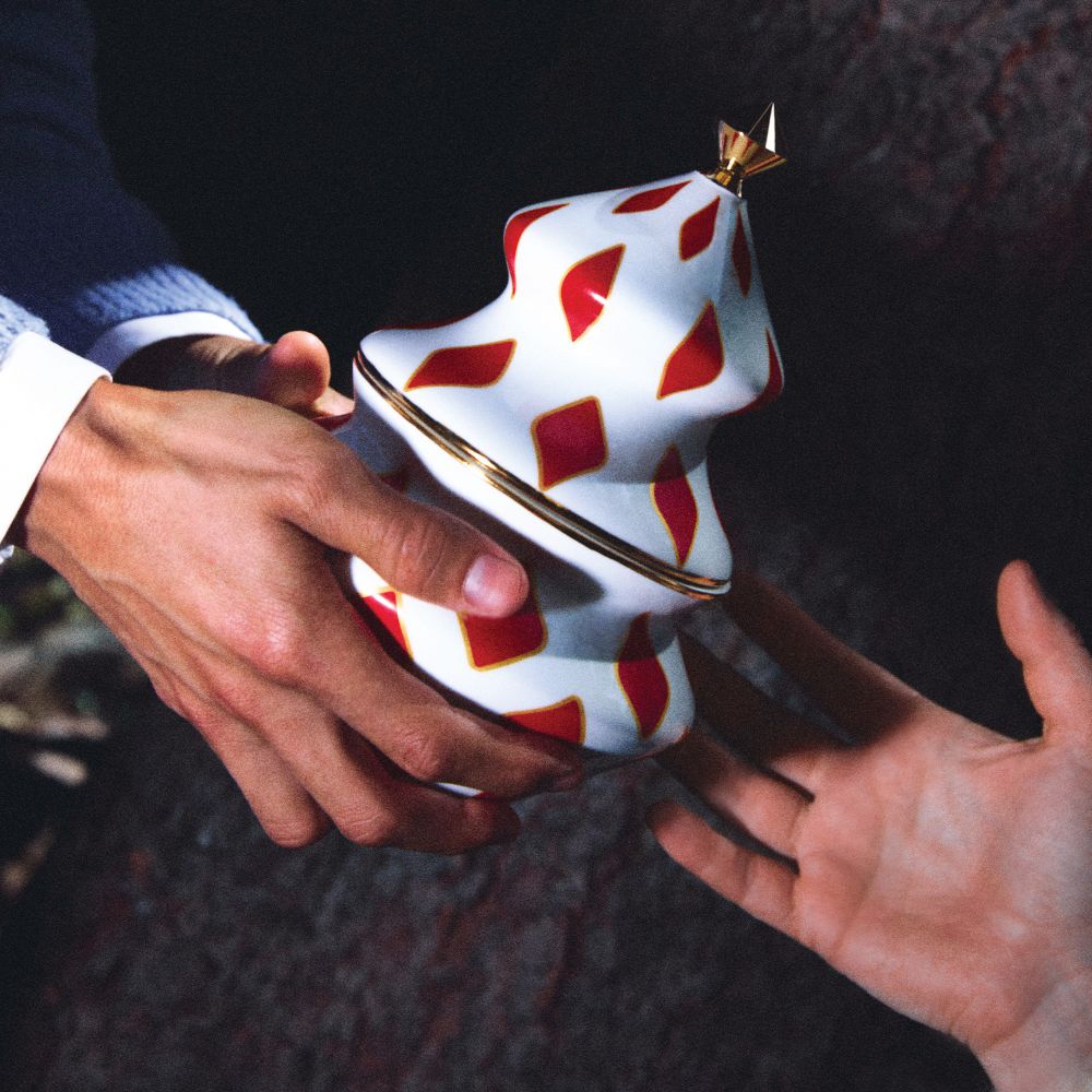 Hände übergeben Alessi Delight Behälter für Süßigkeiten, weiß mit roten Rauten und goldenem Stern.