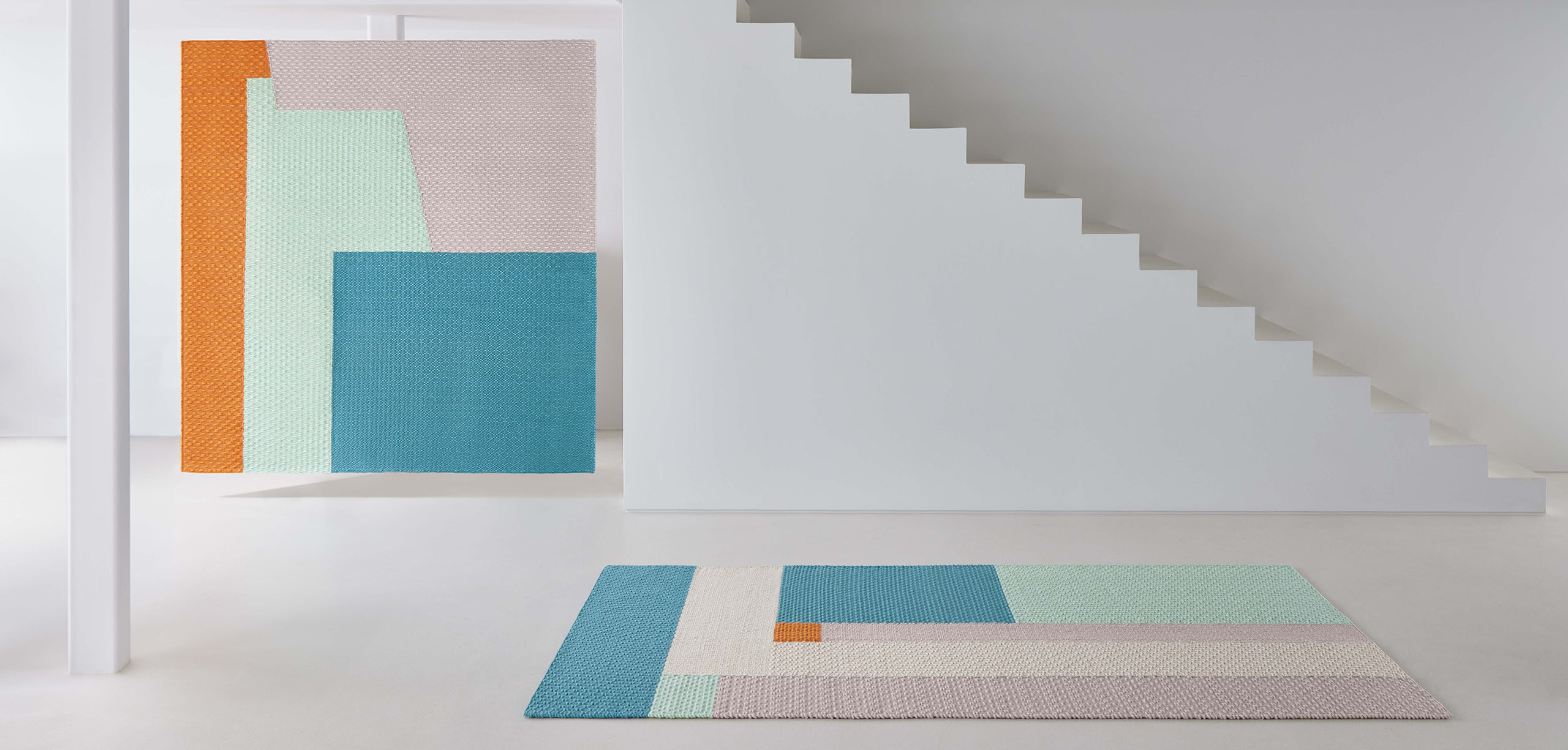 Weave Rug Teppich Space Hopper Gan mit geometrischem Muster in Pastellfarben und Orange in minimalistischem Raum.