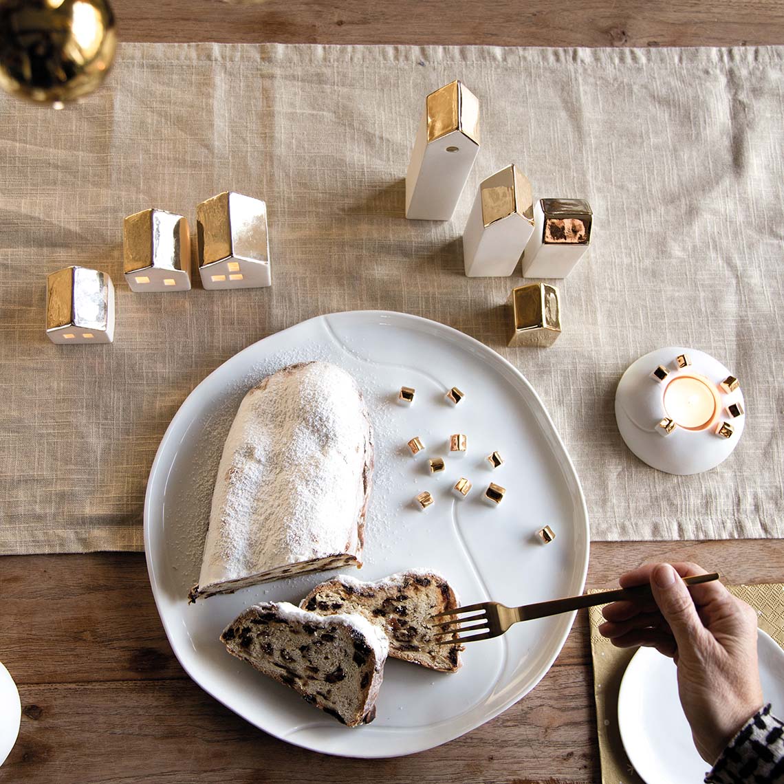 Living Porzellangeschichten Teller mit Stollen, umgeben von goldenen Häusern und Kerzenlicht für festliche Tischdeko.