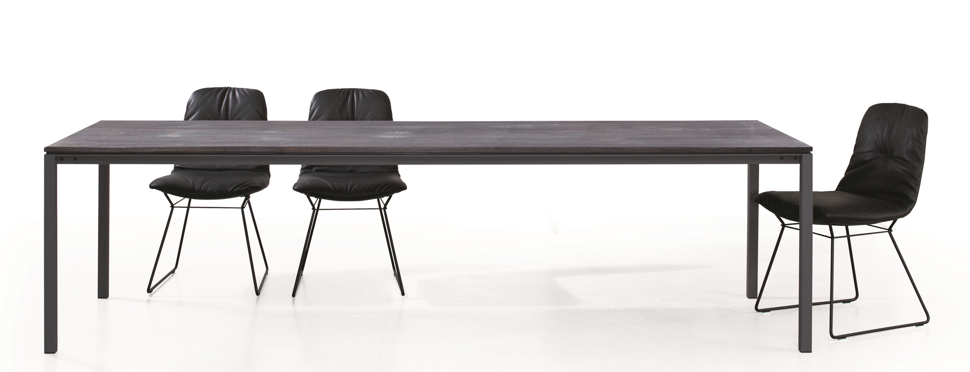 S 600 Tisch von Janua mit geölter Eichenplatte und schwarzen Stühlen vor weißem Hintergrund.