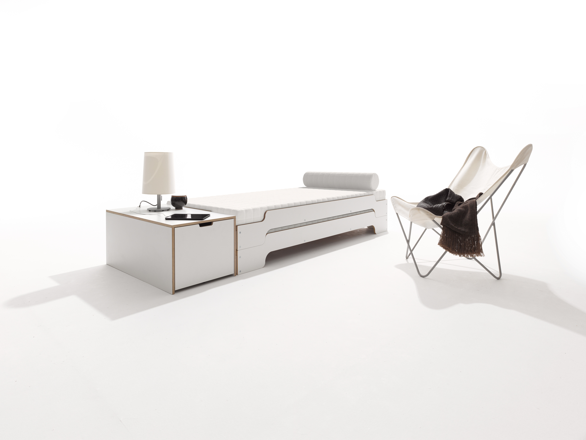 Klassik Bettkasten 16 von Müller Möbelwerkstätten mit Schubkasten, Nachttisch und Sessel auf weißem Hintergrund.