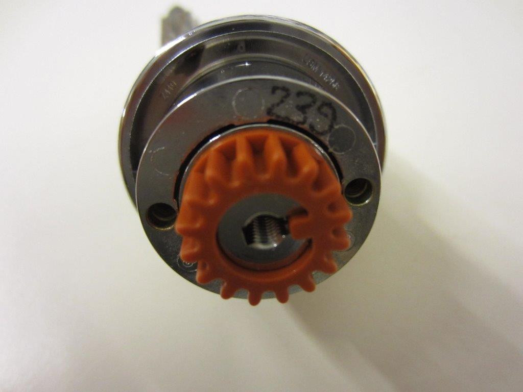Nahaufnahme des USM Haller Schloss Ersatzteils mit orangefarbenem Zahnrad und silberner Mechanik.