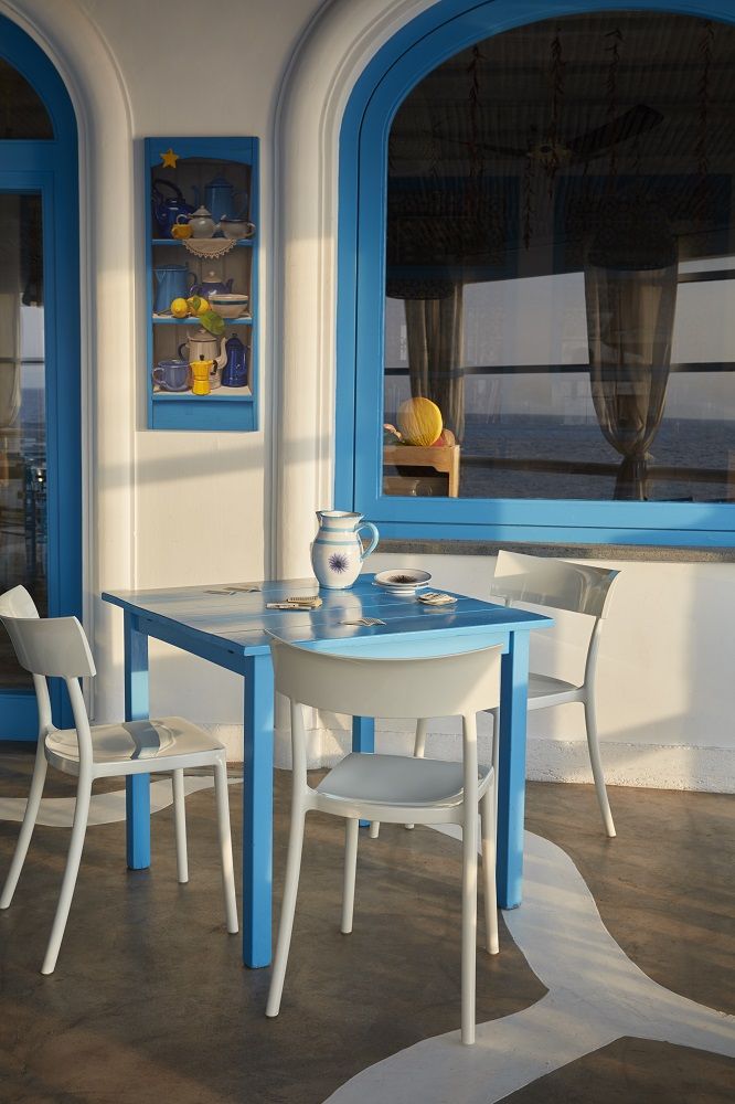 Helle Catwalk Stühle von Kartell um einen blauen Tisch auf einer Terrasse. Designermöbel für den Essbereich.