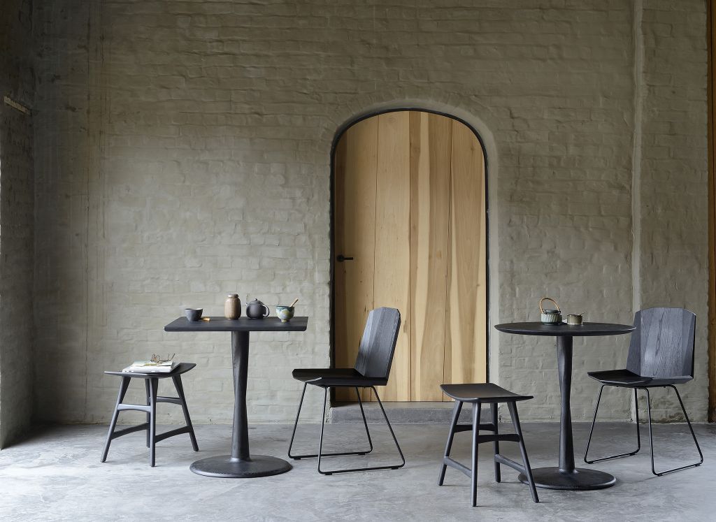Ethnicraft Torsion Eiche Tisch B 70 schwarz mit Stühlen und Hockern vor einer Backsteinwand.
