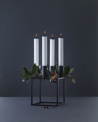 Moderner Adventskranz mit vier weißen Kerzen, schwarzem Metallgestell und grüner Dekoration.