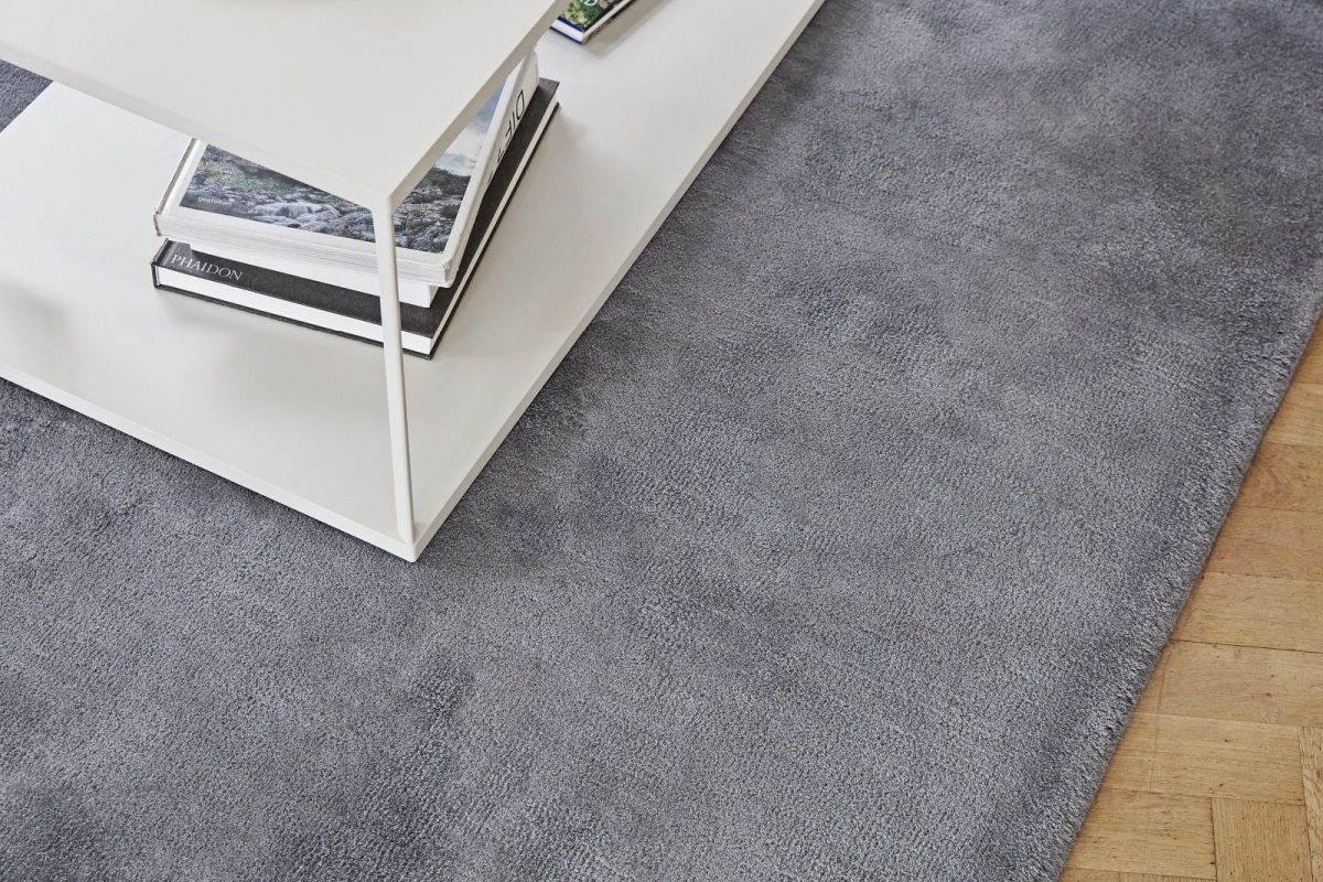 Detailaufnahme eines grauen Teppichs mit kurzem Flor neben einem weißen Couchtisch.