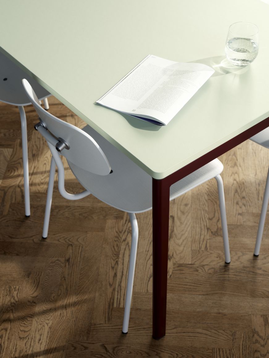 Detailaufnahme eines Kevi Stuhls mit Eichenholz-Sitzfläche und verchromtem Gestell am Tisch. Design Bürostuhl.