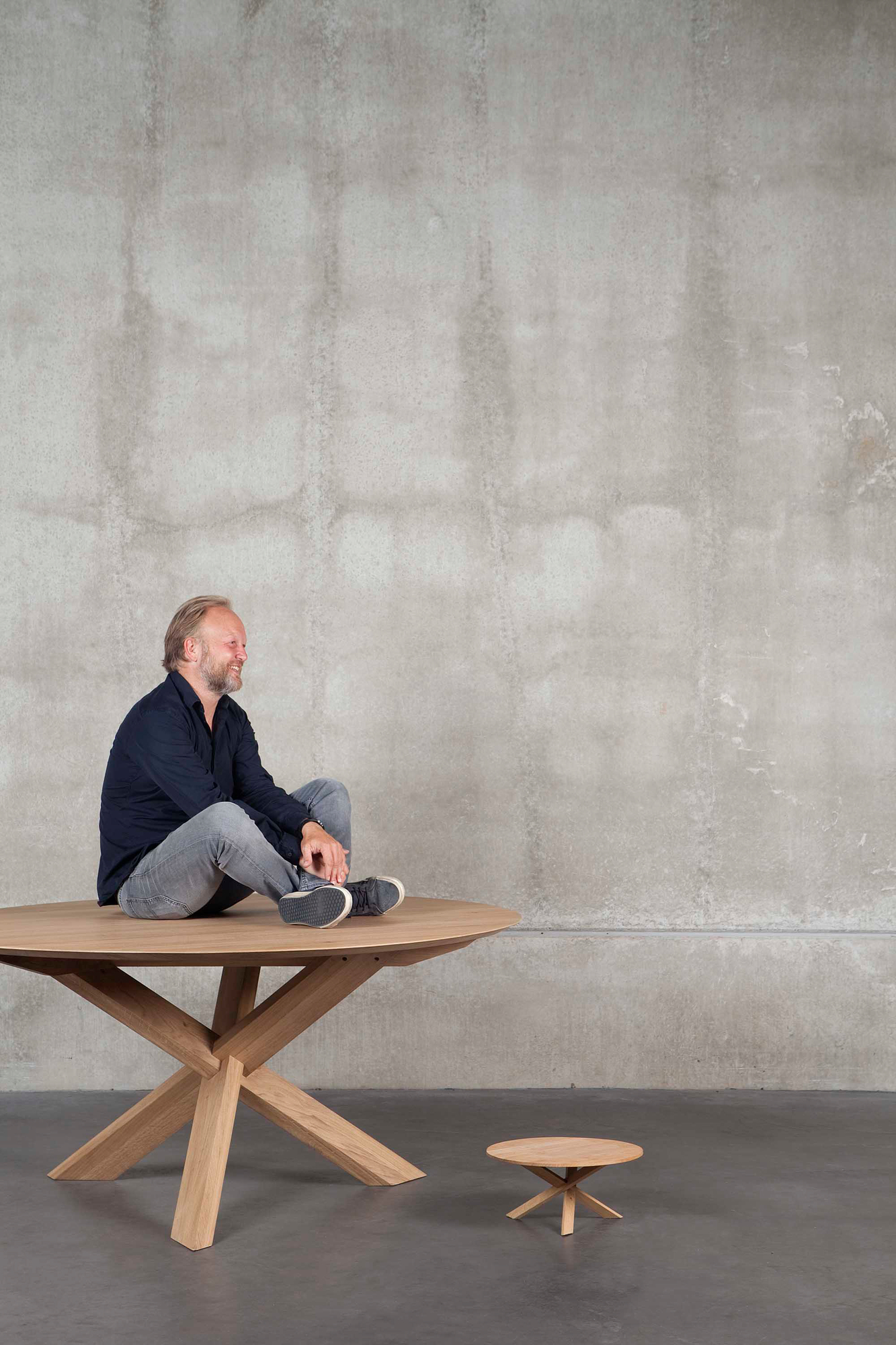 Esstisch Circle von Ethnicraft aus Eiche mit Mann darauf, runder Holztisch mit Kreuzgestell.