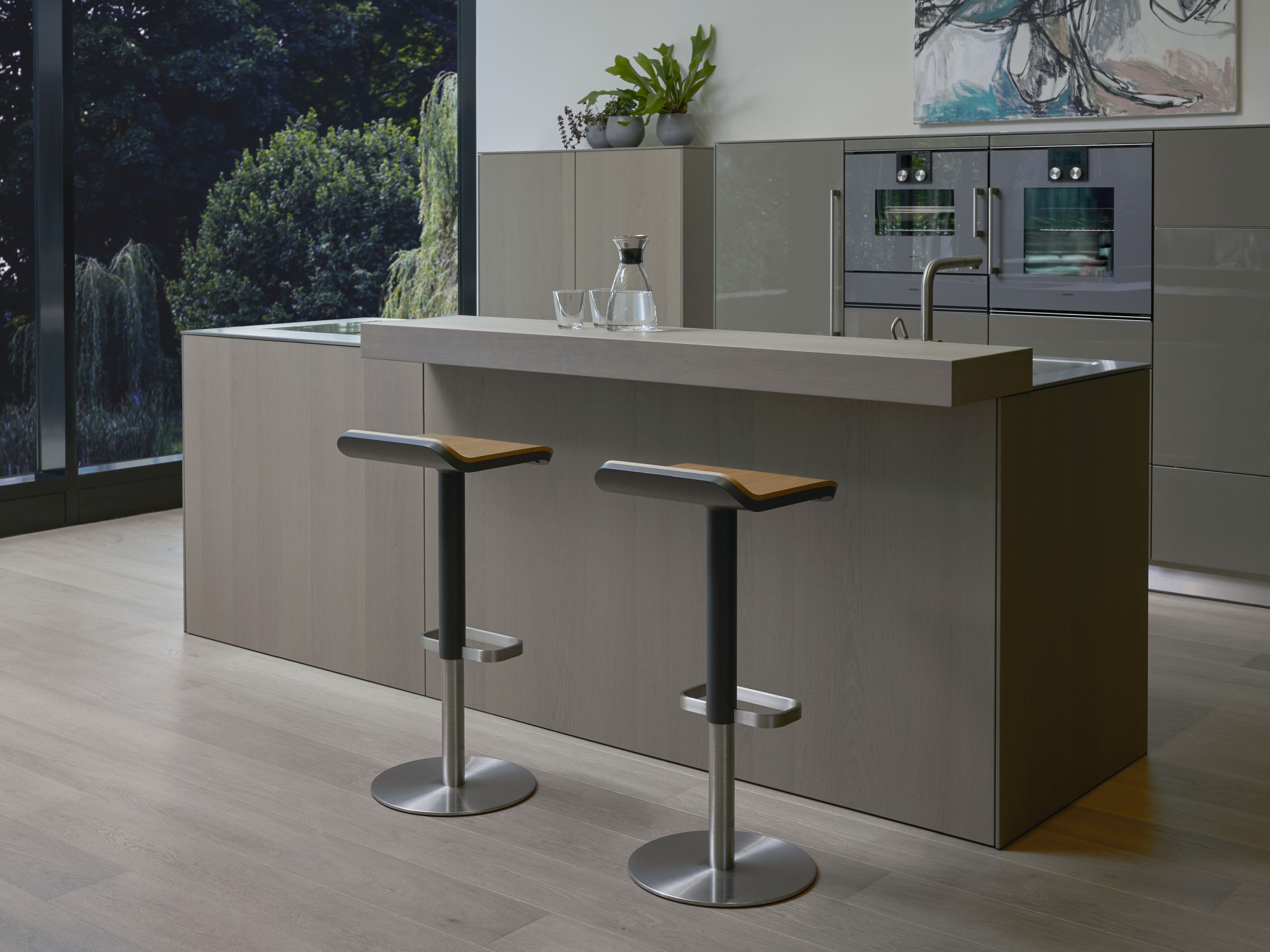 Zwei ED Barhocker mit Edelstahlgestell und Eiche-Sitz vor moderner Kücheninsel. Höhenverstellbare Barstühle für Esszimmer und Küche.