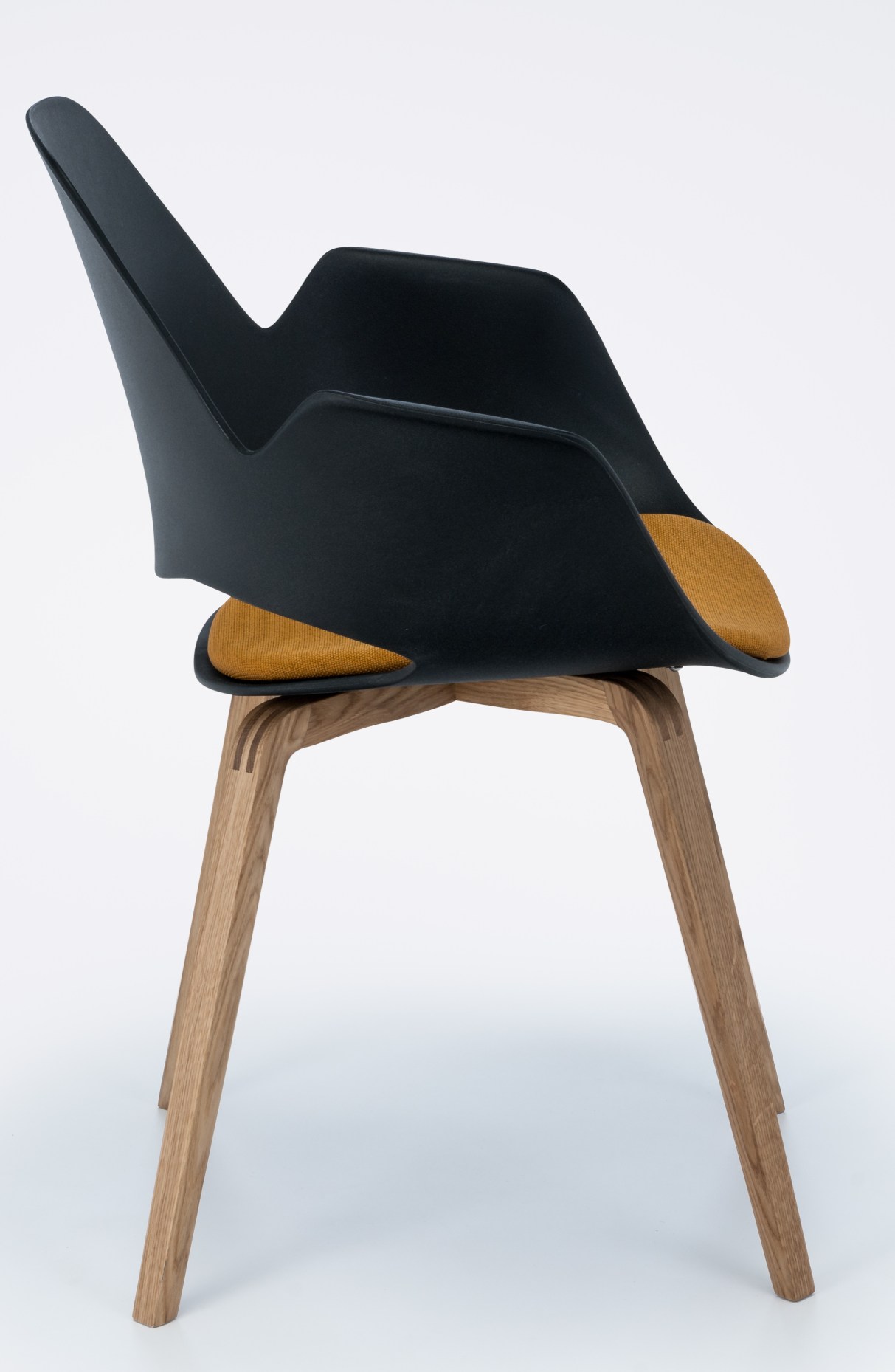 Falk Stuhl von Houe mit Armlehne und Eichenholzbeinen, schwarze Sitzschale und gelbes Sitzkissen.