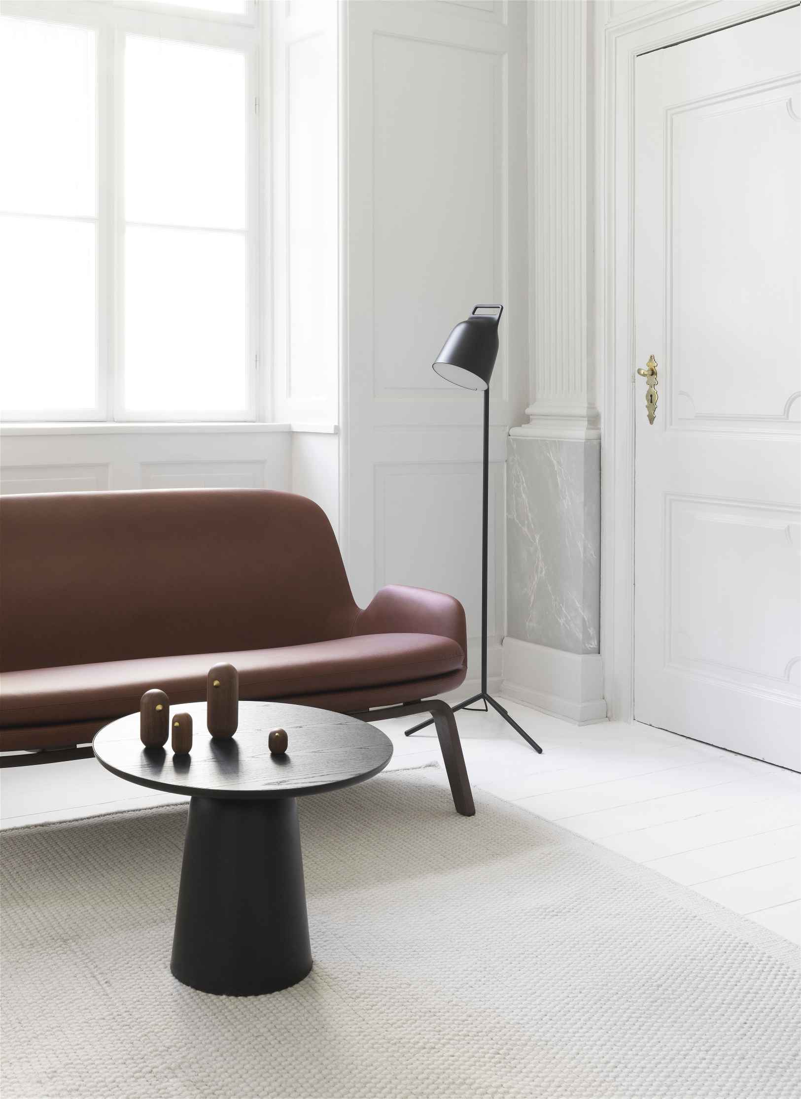 Schwarzer Normann Copenhagen Turn Table Tisch mit Holzfiguren in modernem Wohnzimmer mit Sofa und Stehlampe.